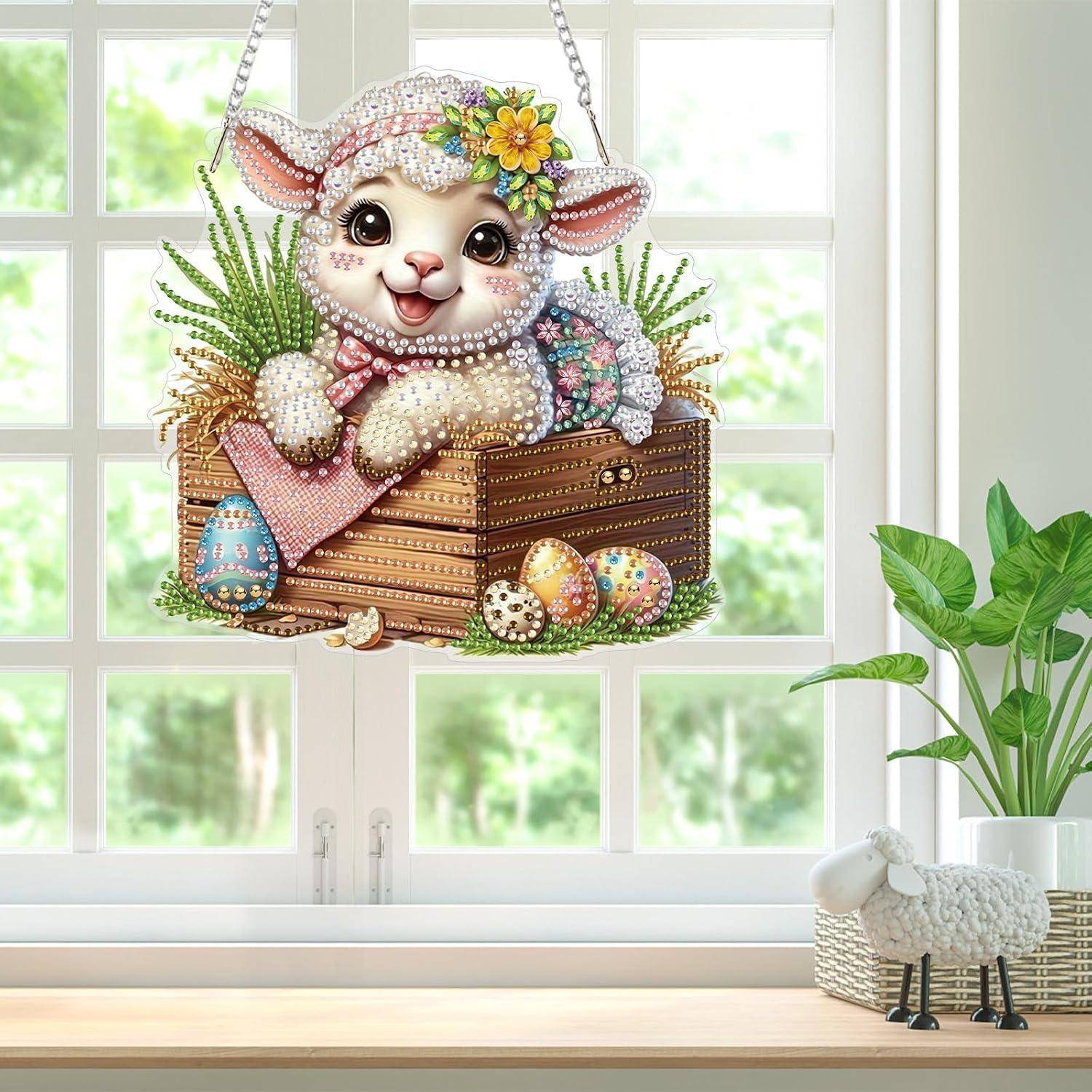 Eine mit Juwelen verzierte Lamm-Dekoration in einem Weidenkorb mit Blumen und Ostereiern hängt vor einem hellen Fenster, mit einer kleinen Schaf-Figur auf der Fensterbank.