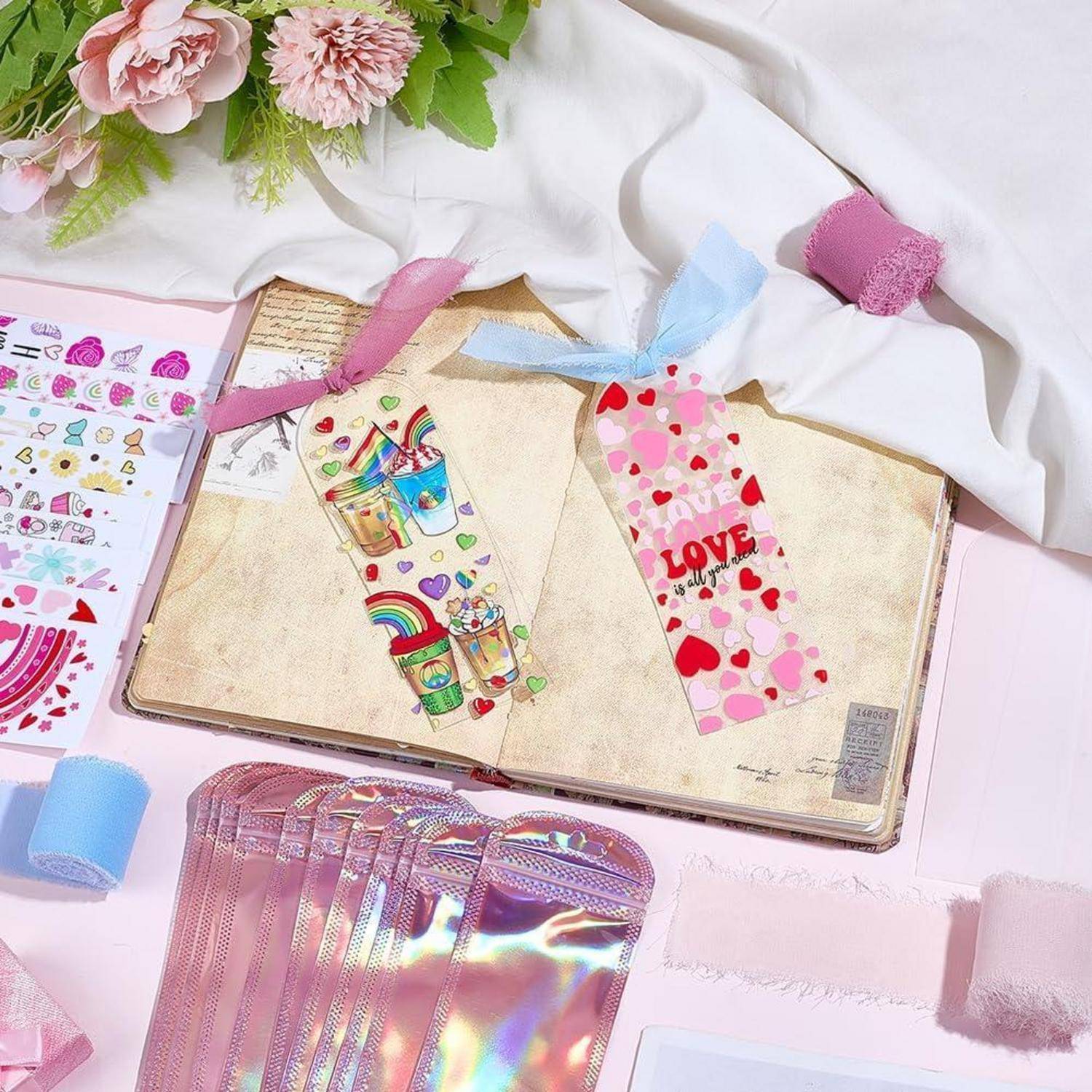 Offenes Scrapbook mit bunten Herz- und Regenbogenstickern, umgeben von Bändern, Klebeband, Blumen und Stickerbogen auf einem pastellfarbenen Basteltisch.
