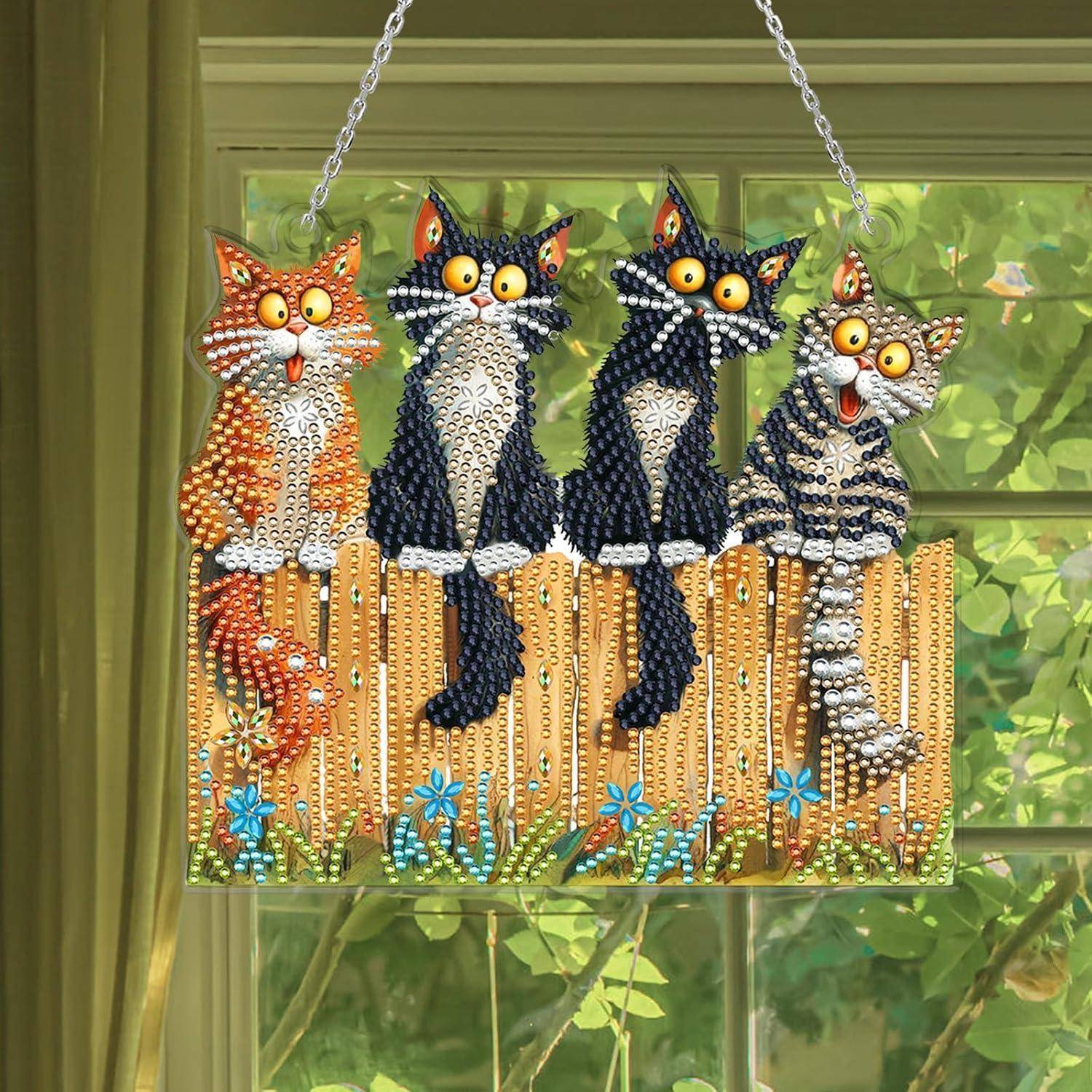 Behängter Wandschmuck aus Perlen mit vier Cartoon-Katzen, die auf einem Zaun sitzen, mit baumelnden Perlensträngen und blauen Blüten, vor einem Fenster mit Grünpflanzen außen.