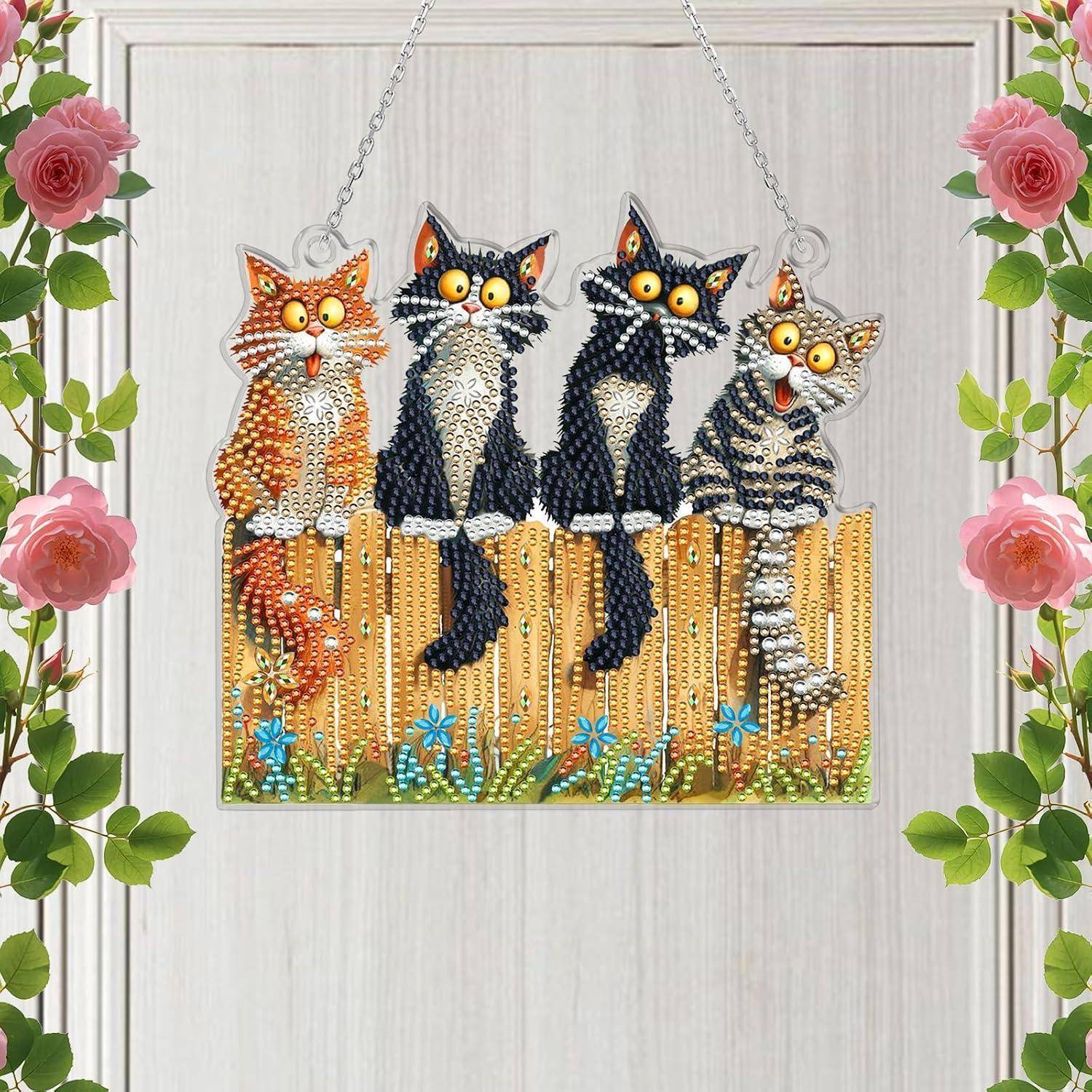 Dekoratives Hängschild mit vier Katzen aus Perlen, die auf einem Zaun sitzen, umrahmt von rosa Rosen und grünen Blättern.