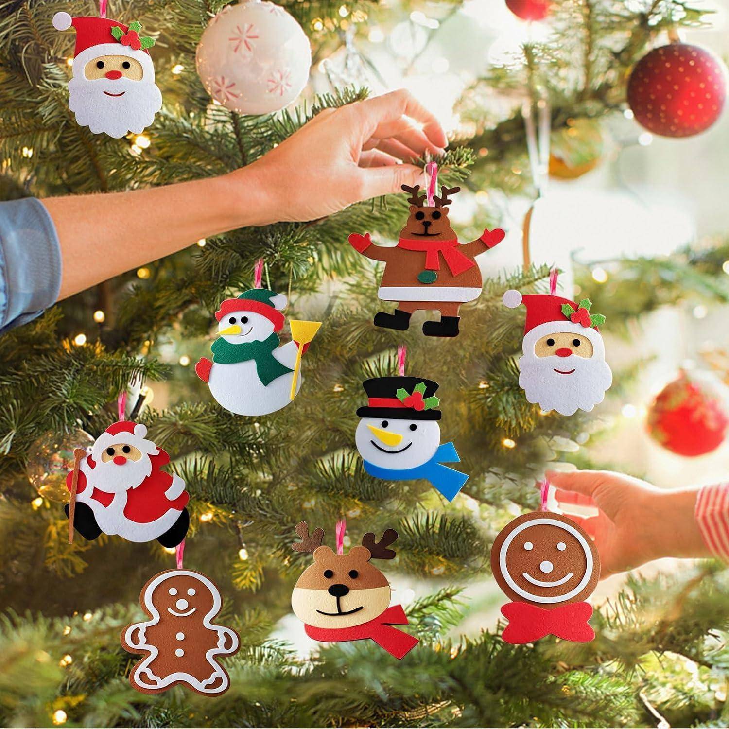 Hände hängen selbstgemachte Weihnachtsfiguren-Ornamente an einen geschmückten Baum auf, darunter den Weihnachtsmann, Schneemänner, ein Lebkuchenmann, ein Rentier und ein Lebkuchengesicht.