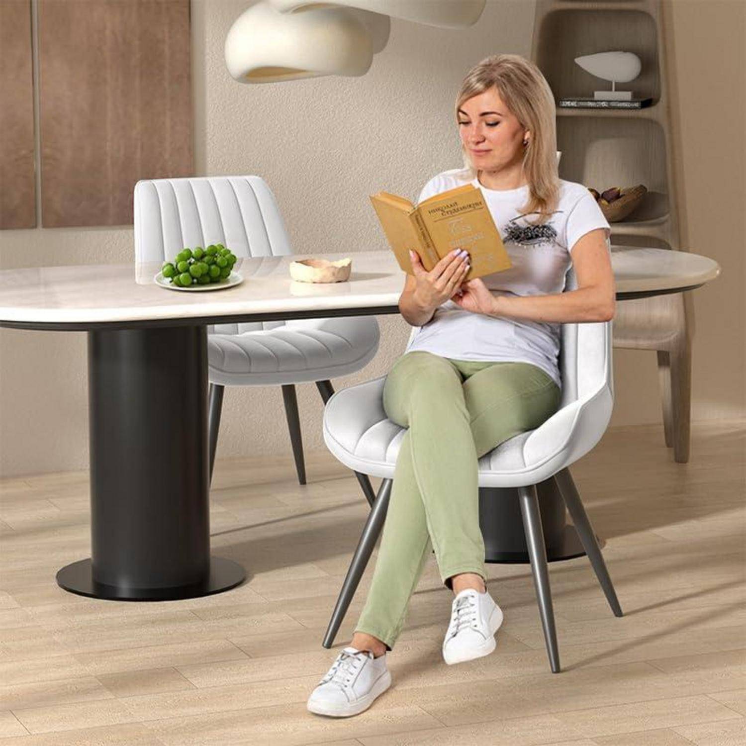 Eine Frau sitzt auf einem weißen Stuhl an einem Esstisch und liest ein Buch in einer modernen Wohnküche oder einem Essbereich.