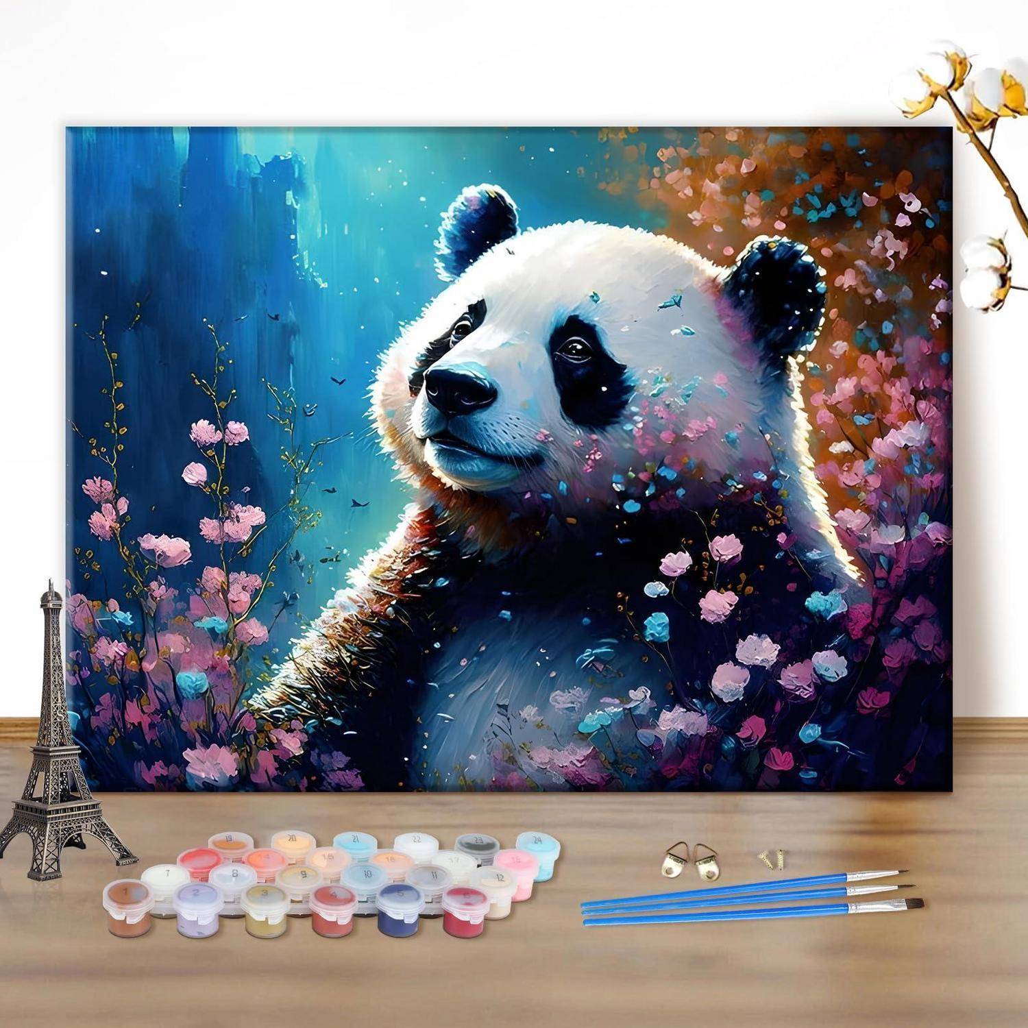 Buntes Pandagemälde auf einer Leinwand in einer floralen blau-rosa Szene, dargestellt auf einer Staffelei mit Farbtöpfen und Pinseln in der Nähe.