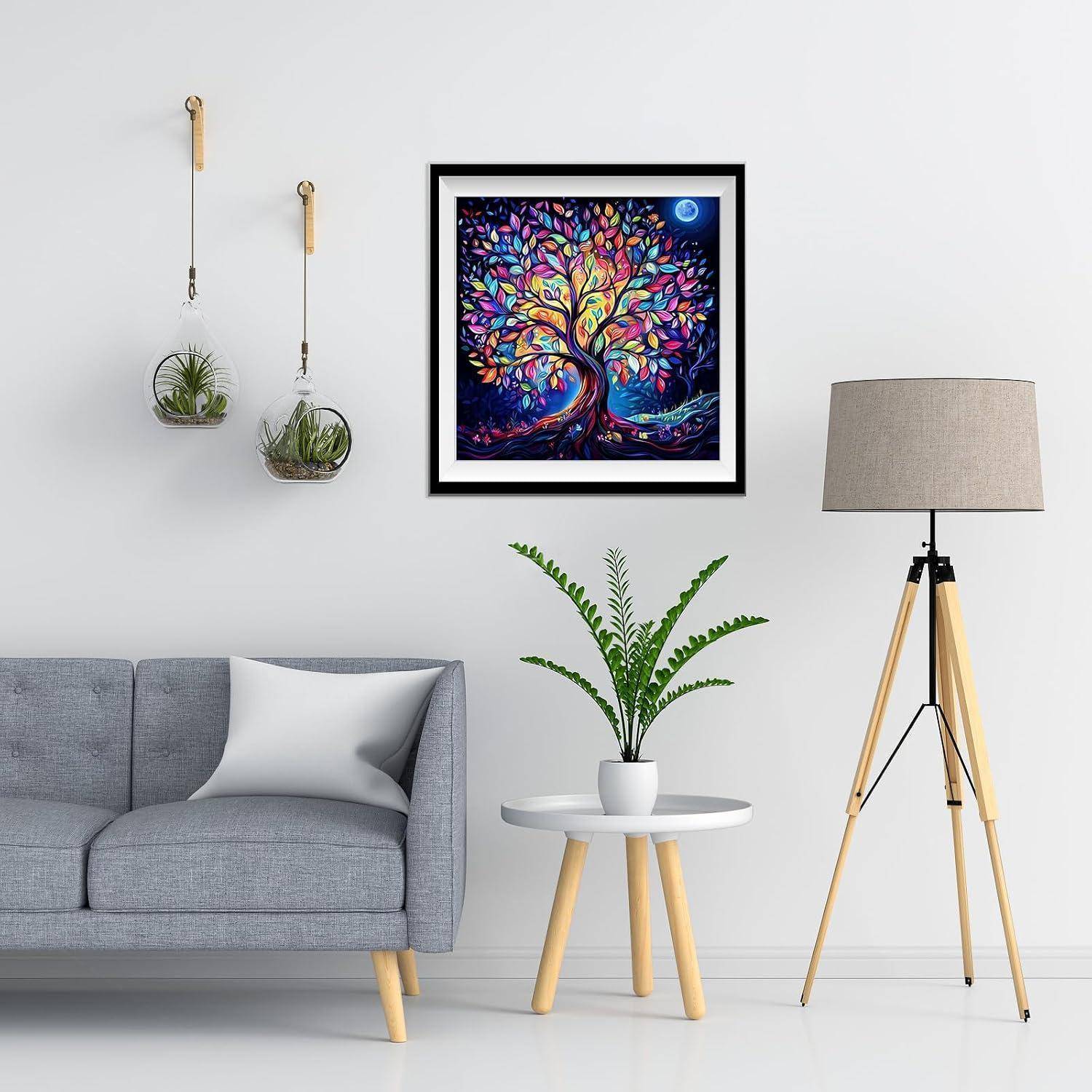 Modernes Wohnzimmer mit grauem Sofa, Topfpflanze auf weißem Tisch, Stativ-Stehleuchte, hängenden Pflanzen und farbigem gerahmtem Baum-Kunstwerk an einer weißen Wand.
