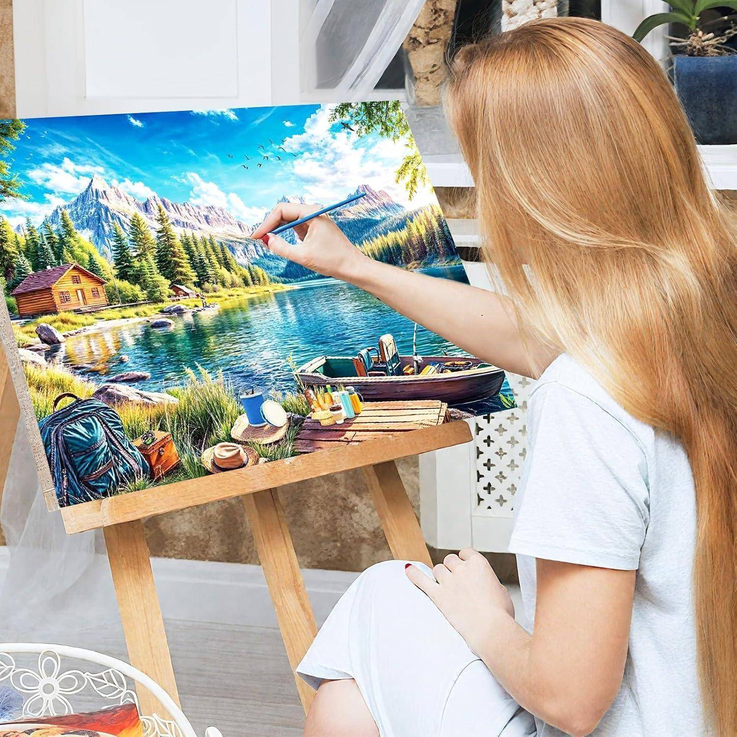 Frau, die eine lebendige Seenlandschaft auf einer Staffelei malt, mit Bergen, Bäumen, Hütte, Boot und Picknick-Szene im Kunstwerk.