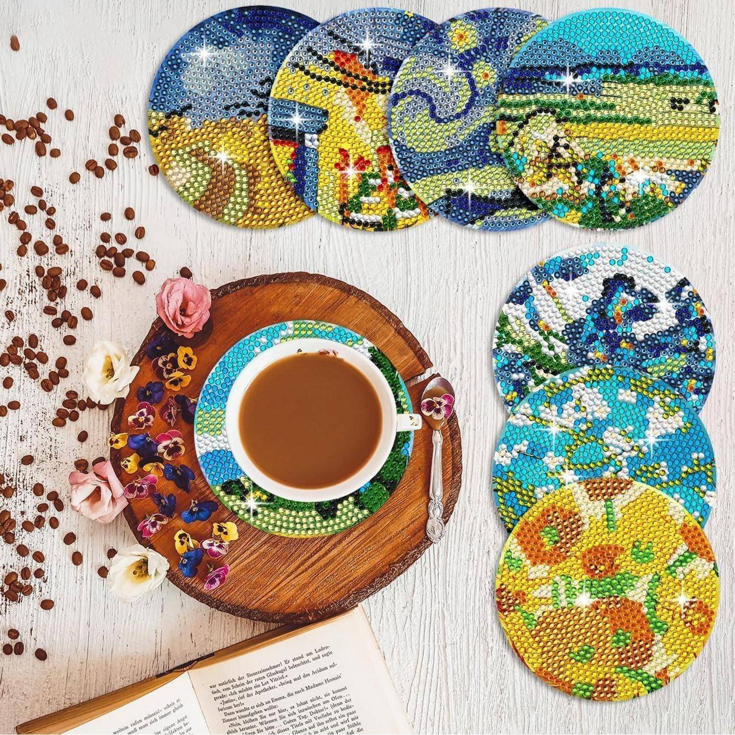 Kaffeetasse auf einer hölzernen Untertasse mit Blumen und verstreuten Bohnen, neben bunten runden Perlenuntersetzern und einem aufgeschlagenen Buch auf einem weißen Tisch.