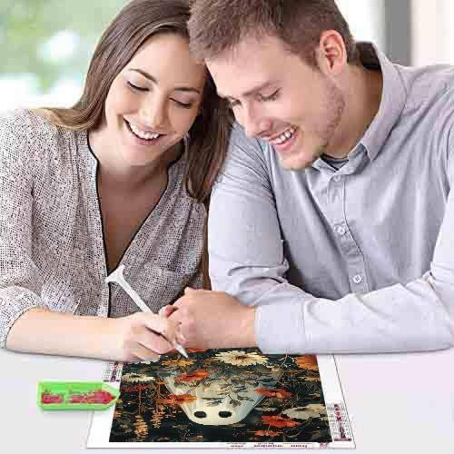 Lachendes Paar, das sich über einen Tisch beugt und gemeinsam an einem Foto oder Kunstdruck mit einem Stift arbeitet, konzentriert auf das Projekt zusammen.
