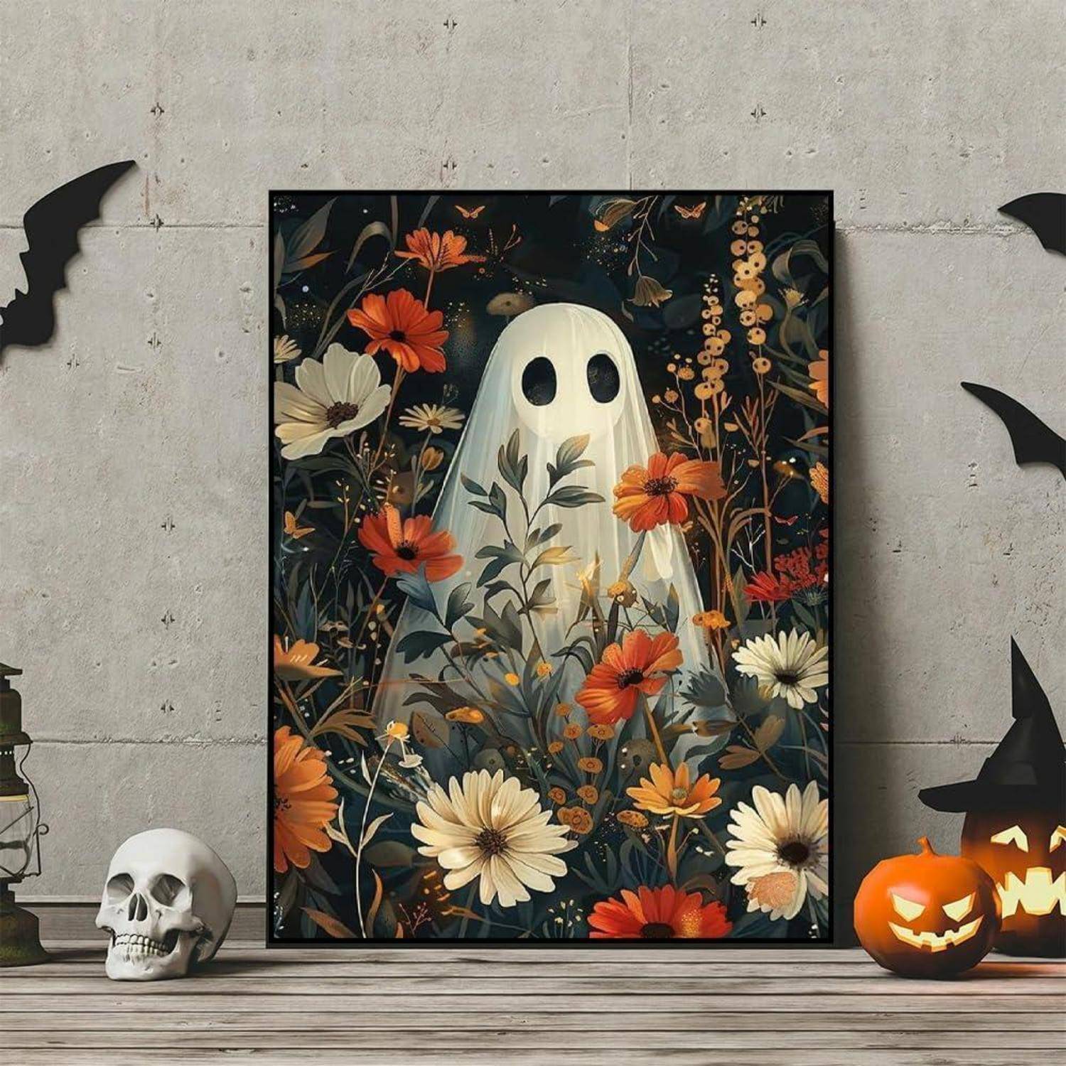 Gerahmtes Halloween-Poster mit einem weißen Gespenst zwischen Blumen, mit geschnitzten Kürbissen, Fledermäusen und einem Schädel auf einem Holzboden vor einer Betonwand.