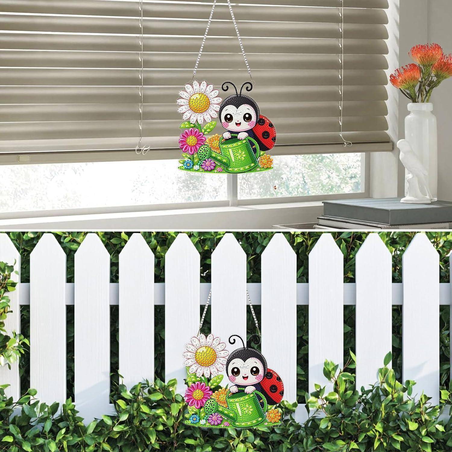 Bunte Marienkäfer- und Blumenhängdekoration, die an einem Fenster und einem weißen Lattenzaun angebracht ist, mit einer Vase und Büchern in der Nähe.