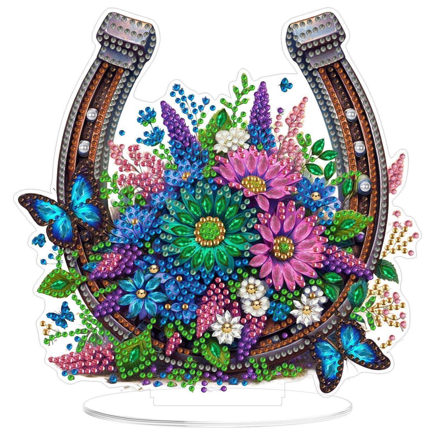 Farbenfrohe, mit Edelsteinen besetzte, hufeisenfrmige Blumenornament mit Schmetterlingen und funkelnden Perlendetails auf einem Ausstellungsständer.