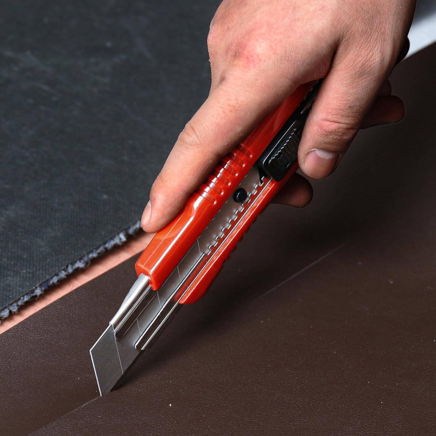 Eine Hand benutzt ein rotes Universalmesser, um braunes Material entlang einer geraden Kante auf einer dunklen Arbeitsfläche durchzuschneiden.