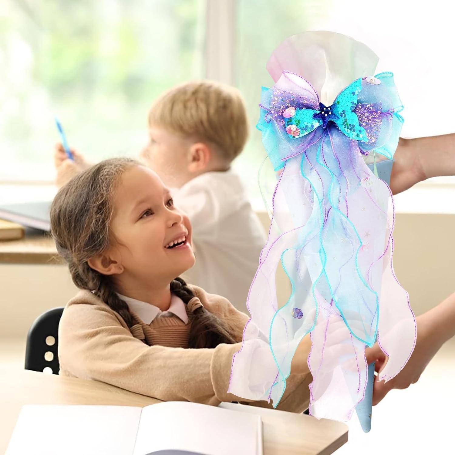 Ein lächelndes Schulmädchen beobachtet ein buntes, quallenenförmiges Kunstwerk mit fließenden Bändern, das in einem Klassenzimmer hochgehalten wird.