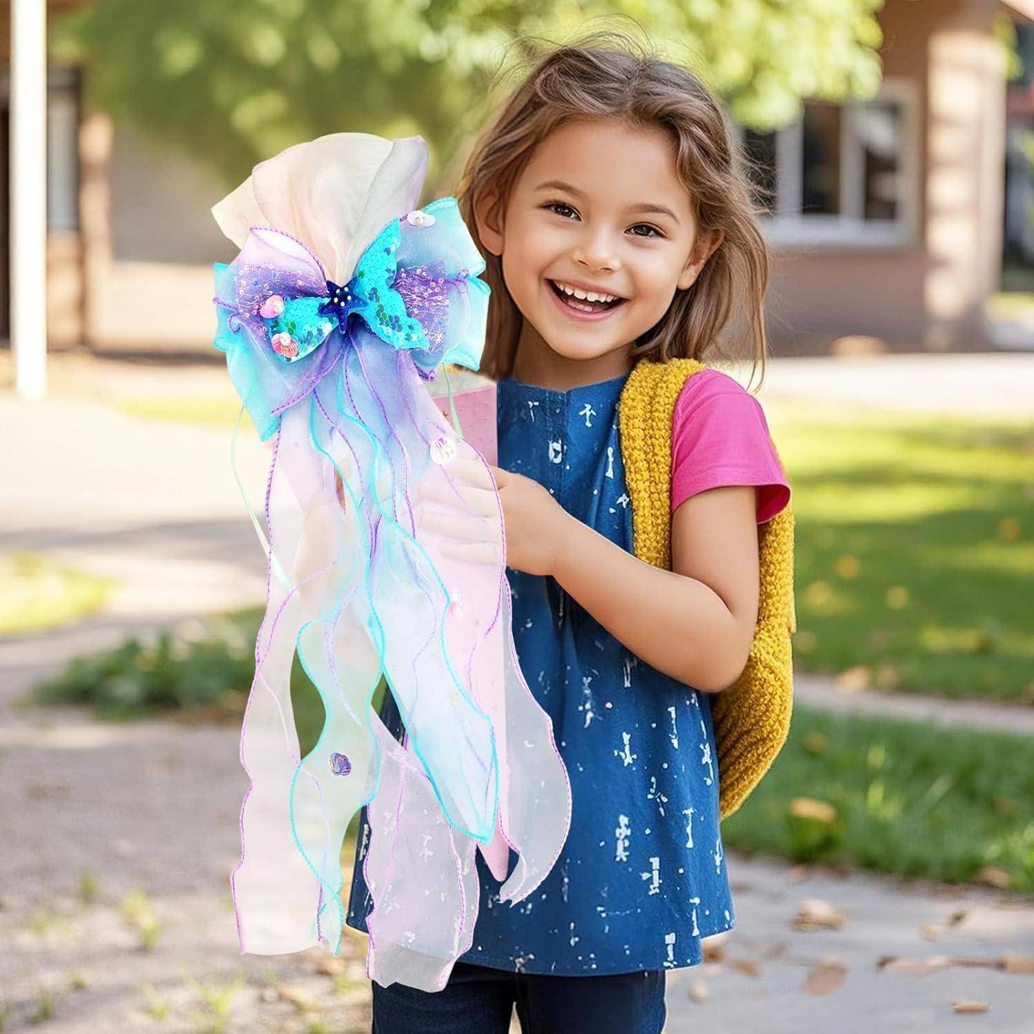 Lächelndes junges Mädchen in einem blauen Kleid mit einem gelben Rucksack hält einen bunten, handgefertigten Schleifen- oder Zauberstab im Freien auf einem Gehweg.
