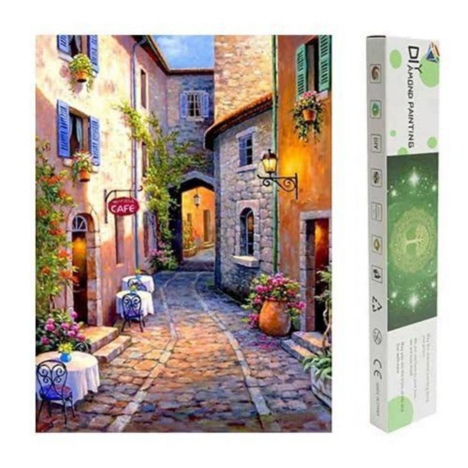 Diamantmalerei-Set in einer Schachteln mit einem bunten Kopfsteinpflaster-Gässchen mit einem Café, blumigen Fenstern und Steingebäuden.