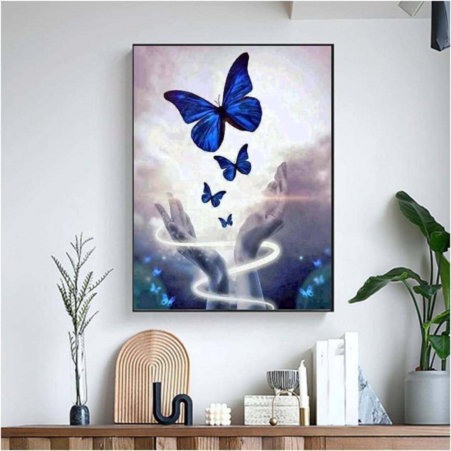 Gerahmte Wandkunst mit blauen Schmetterlingen über ausgestreckten Händen mit einer leuchtenden Spirale, ausgestellt auf einem Regal in einem modernen Zimmer.