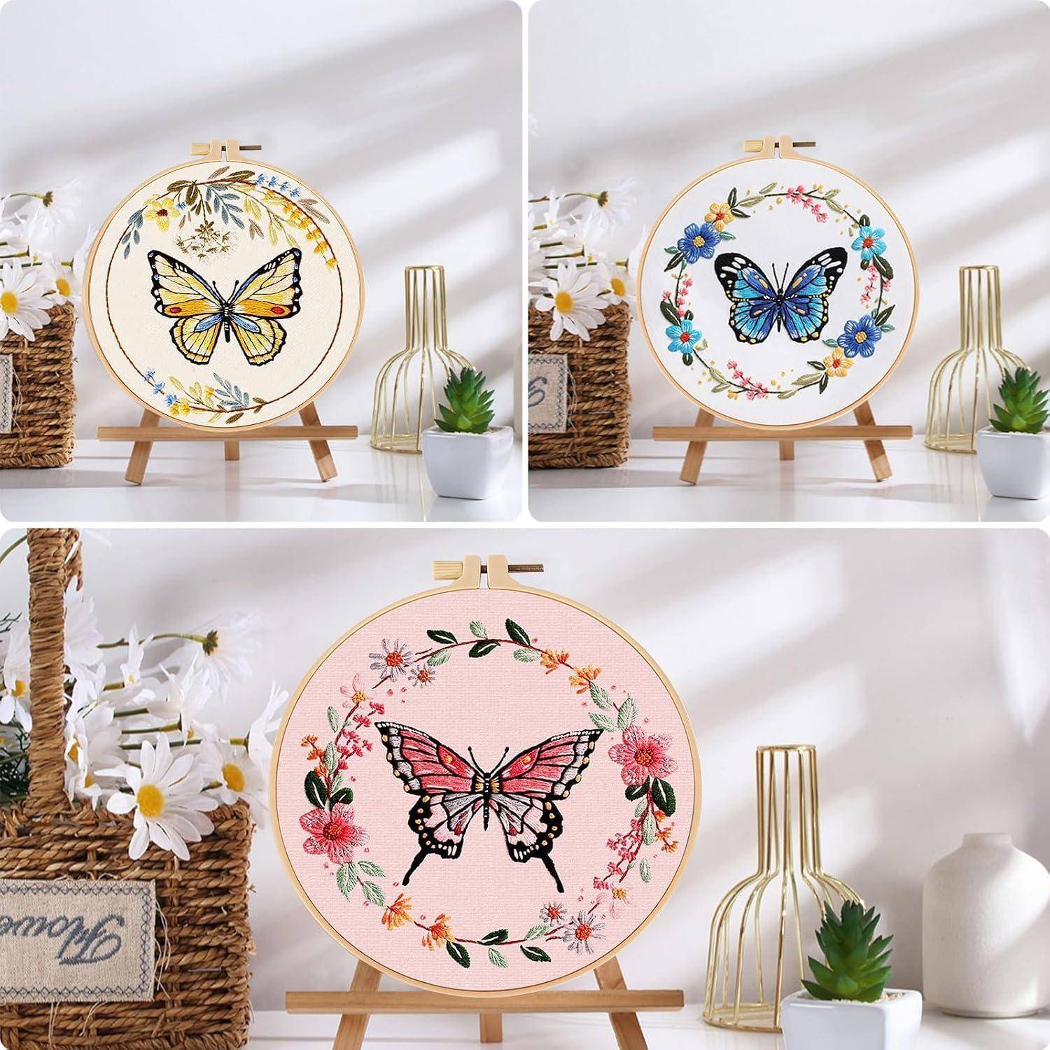 Drei bestickte Reifen-Kunstwerke auf Ständern, jedes mit einem Schmetterlings-Design und Blumenkranz, gezeigt als dekorative Wand- oder Regaldekoration.