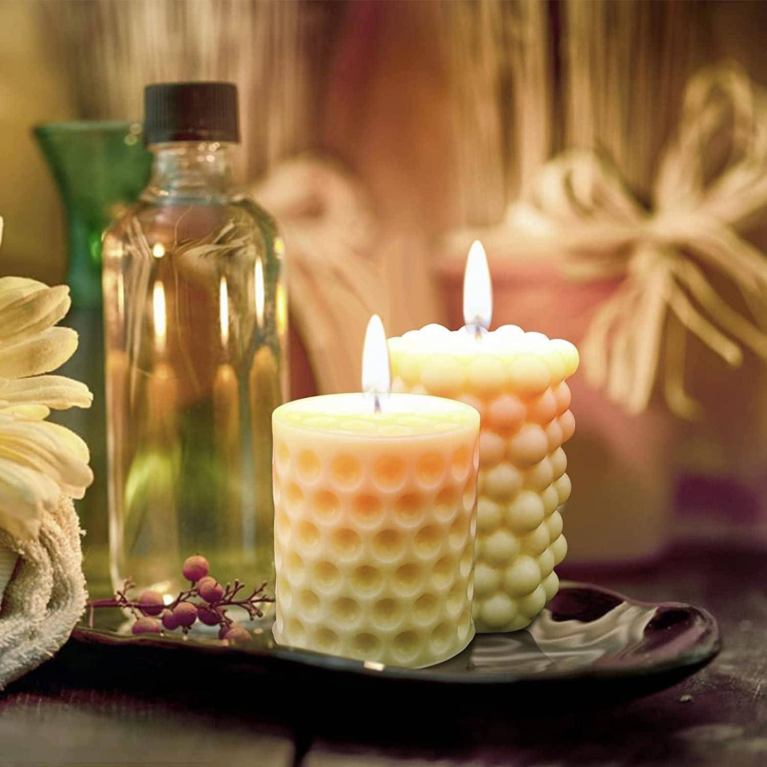 Zwei brennende Wabkerzen auf einem schwarzen Tablett neben einer Glasflasche und Blumen, die eine warme spa-ähnliche Anzeige schaffen.