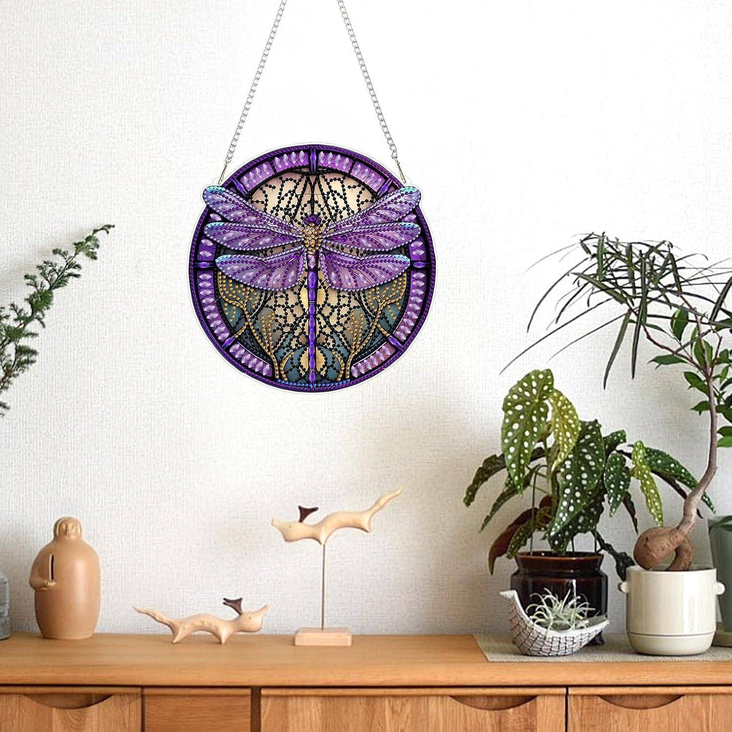 Violetter Schmetterling aus Buntglas als Wandbehang, zentriert über einem Holz-Sideboard mit Topfpflanzen und kleinen Dekorationsobjekten.