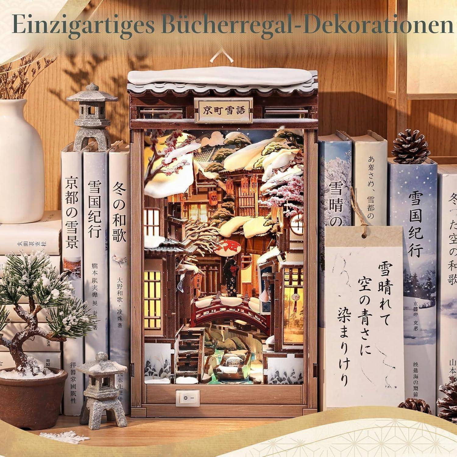 Verziertes Bücherregal mit japanisch gestalteten Buchstützen, Büchern, einer Miniatur-Tempelszene, Tannenzapfen und einer Pflanze auf einem Holzregal.