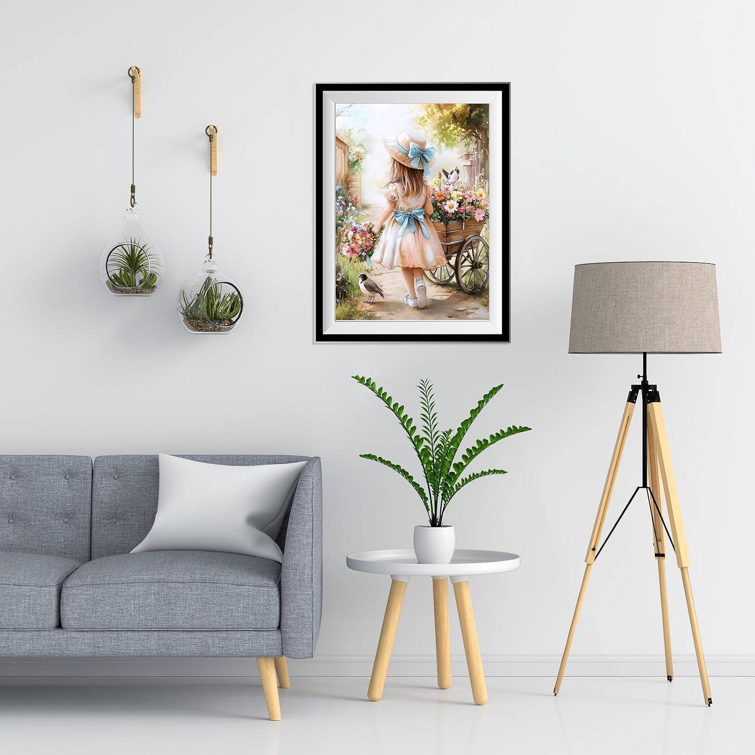 Stilvolles Wohnzimmer mit grauem Sofa, Beistelltisch und Pflanze, Stativstehlampe, hängenden Blumenkübeln und Wandkunst in Rahmen an einer weißen Wand.