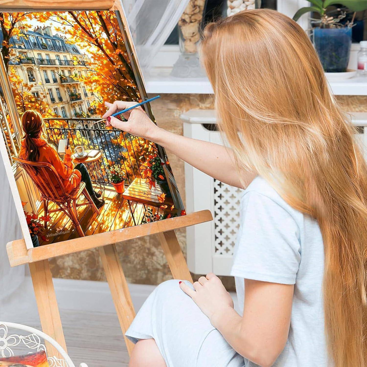 Eine Frau malt eine Herbstszene auf einem Balkon auf einer Staffelei, mit einer sitzenden Figur und Stadtgebäuden, die von orangefarbenen Blättern eingerahmt sind.