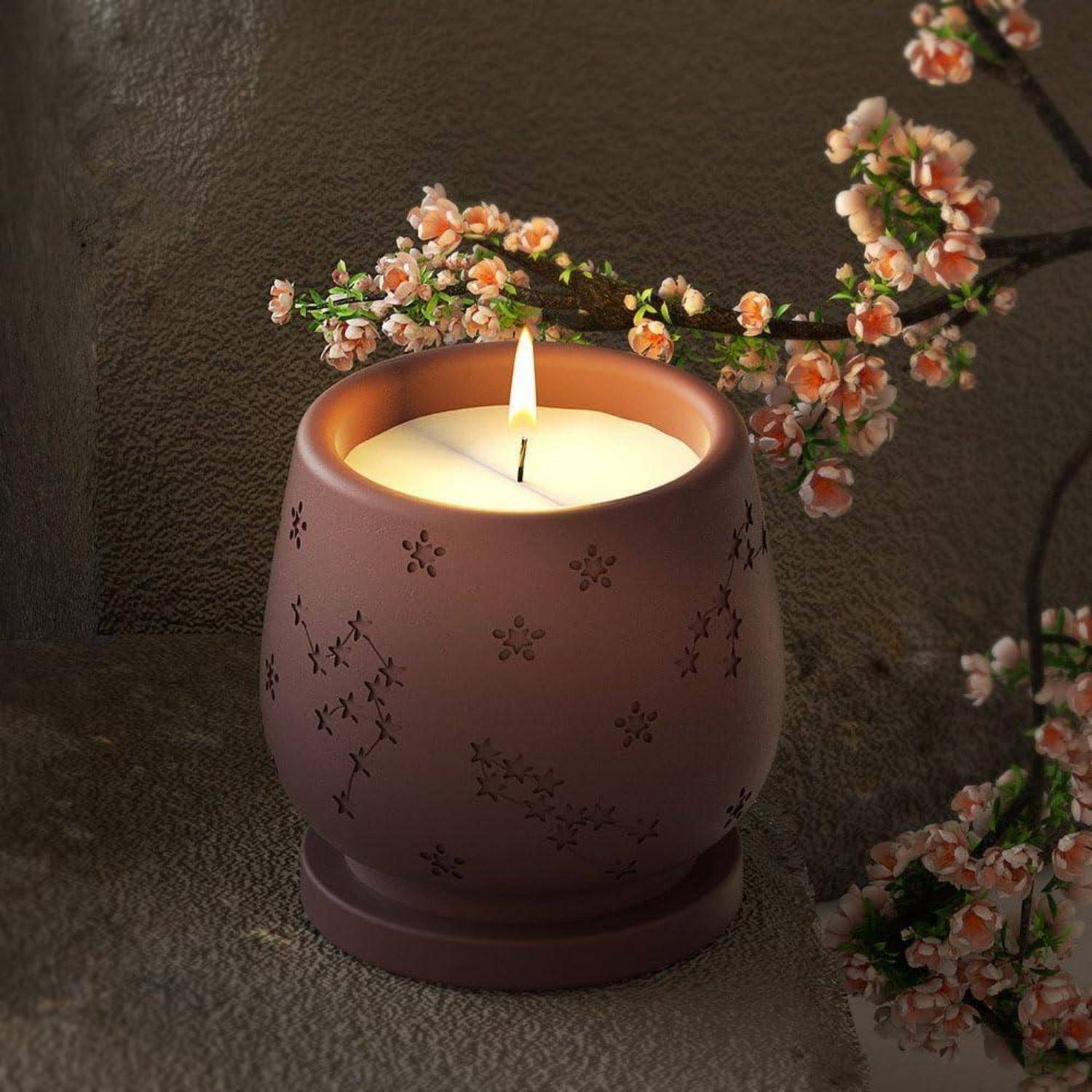Brennende Kerze in einem mauve-farbenen dekorativen Keramikhalter, umgeben von rosa Blüten auf einer strukturierten Oberfläche.