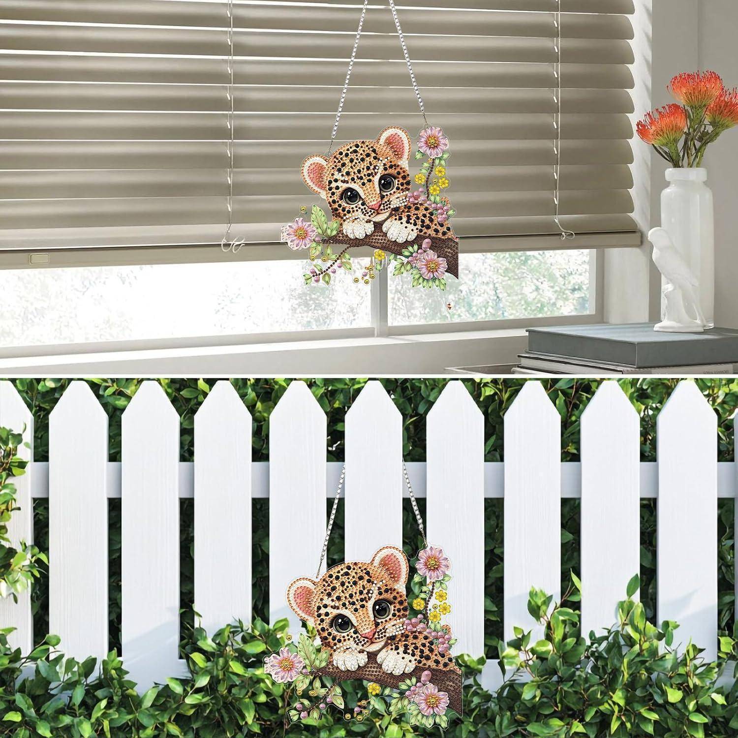 Leopardenjunges hängende dekorative Verzierung mit Blumen, gezeigt im Innenbereich neben einem Fenster und im Außenbereich an einem weißen Lattenzaun.
