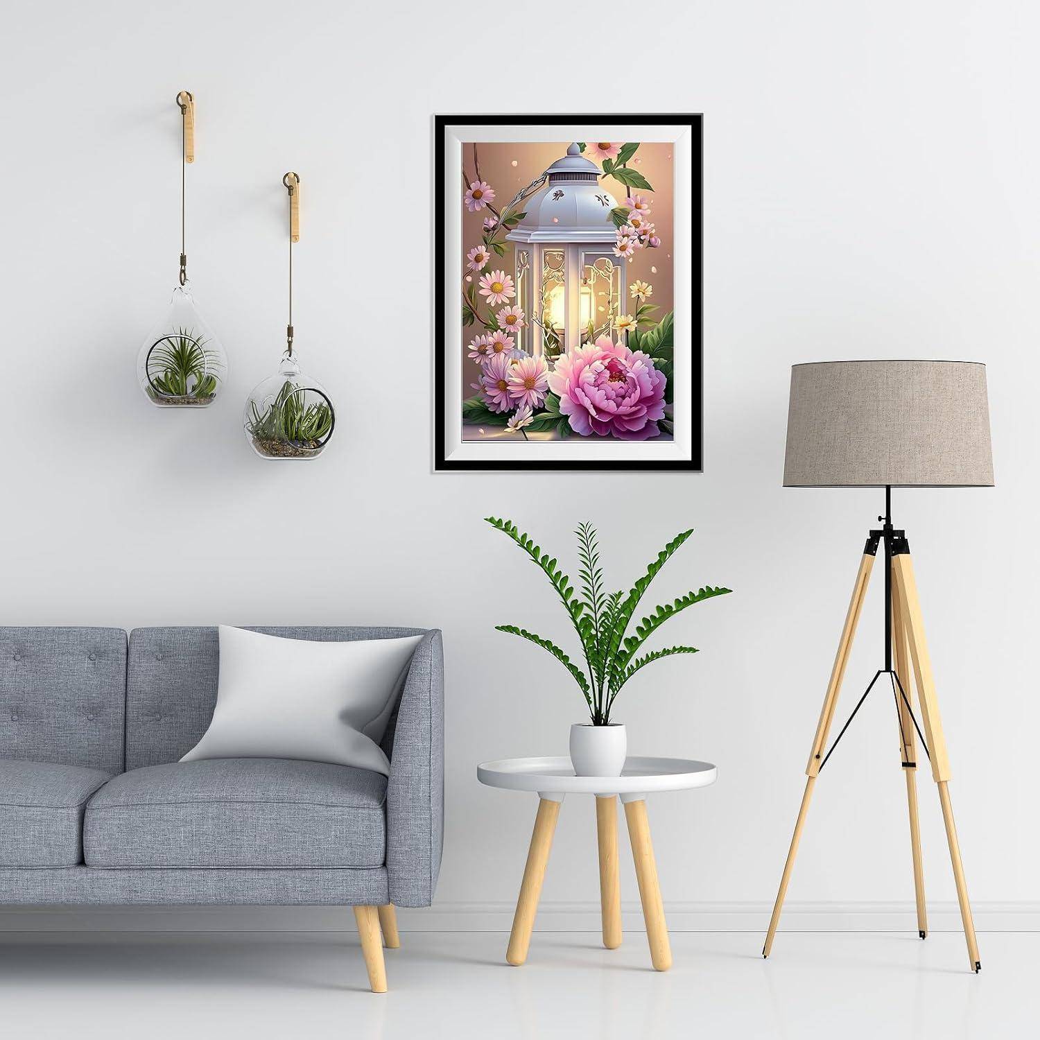 Modernes Wohnzimmer mit grauem Sofa, gerahmtem Blumen-Laternenbild, hängenden Pflanzen, Topfpflanze auf dem Beistelltisch und Dreibein-Stehleuchte.