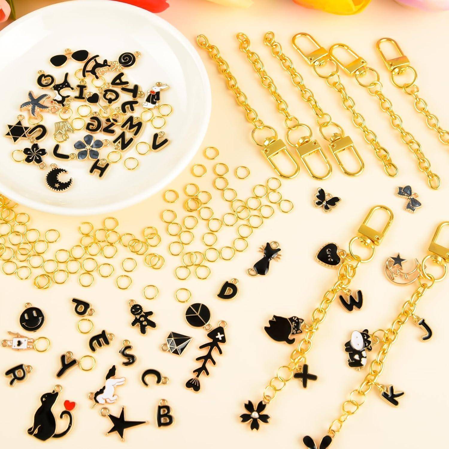 Assortierte Gold- und Schwarz-Schmuckanhänger, Buchstabenkugeln und Kettenverschlüsse auf hellem Hintergrund in einer Bastelwerkstatt-Ausstellung angeordnet.