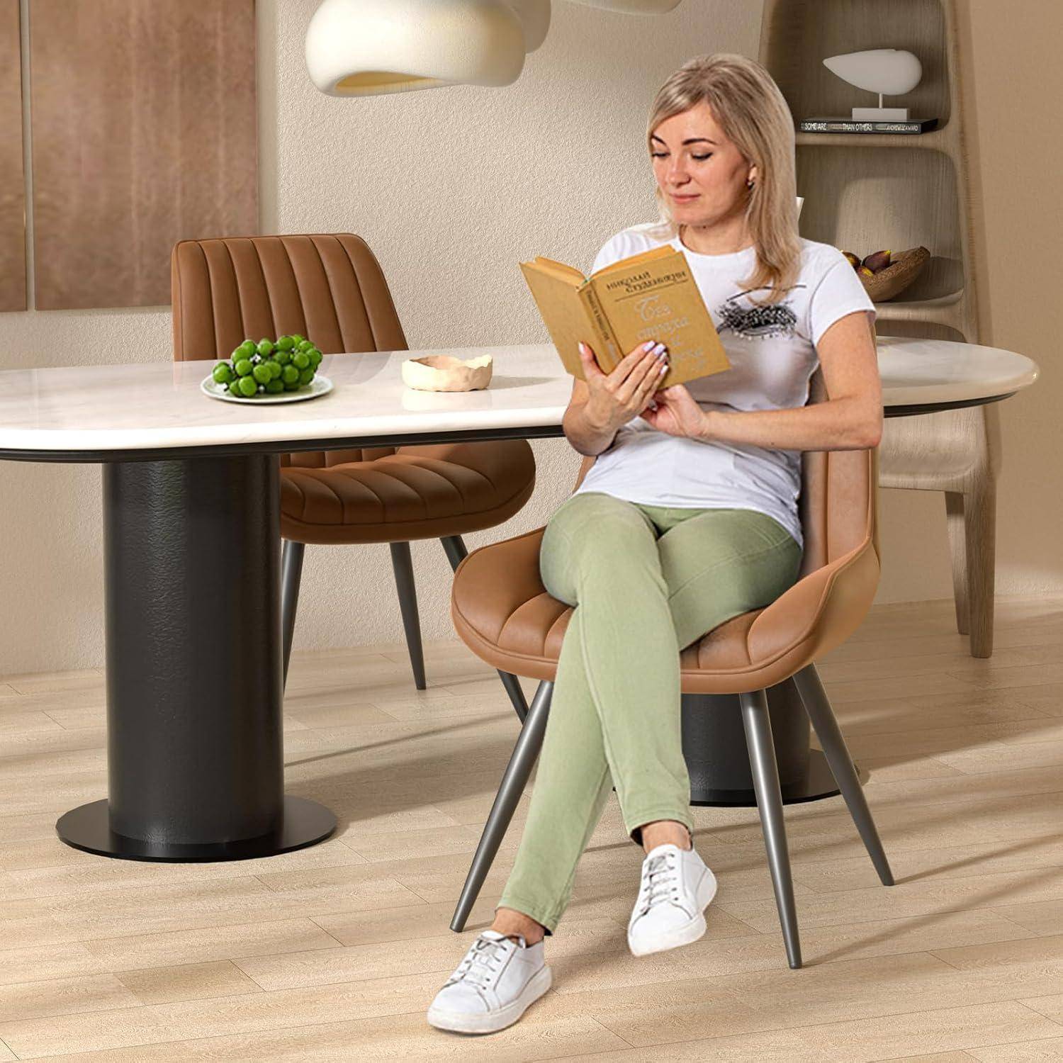 Frau, die an einem Esstisch in einem modernen Zimmer sitzt, liest ein Buch neben einem Teller mit Trauben und einem Stück Kuchen.