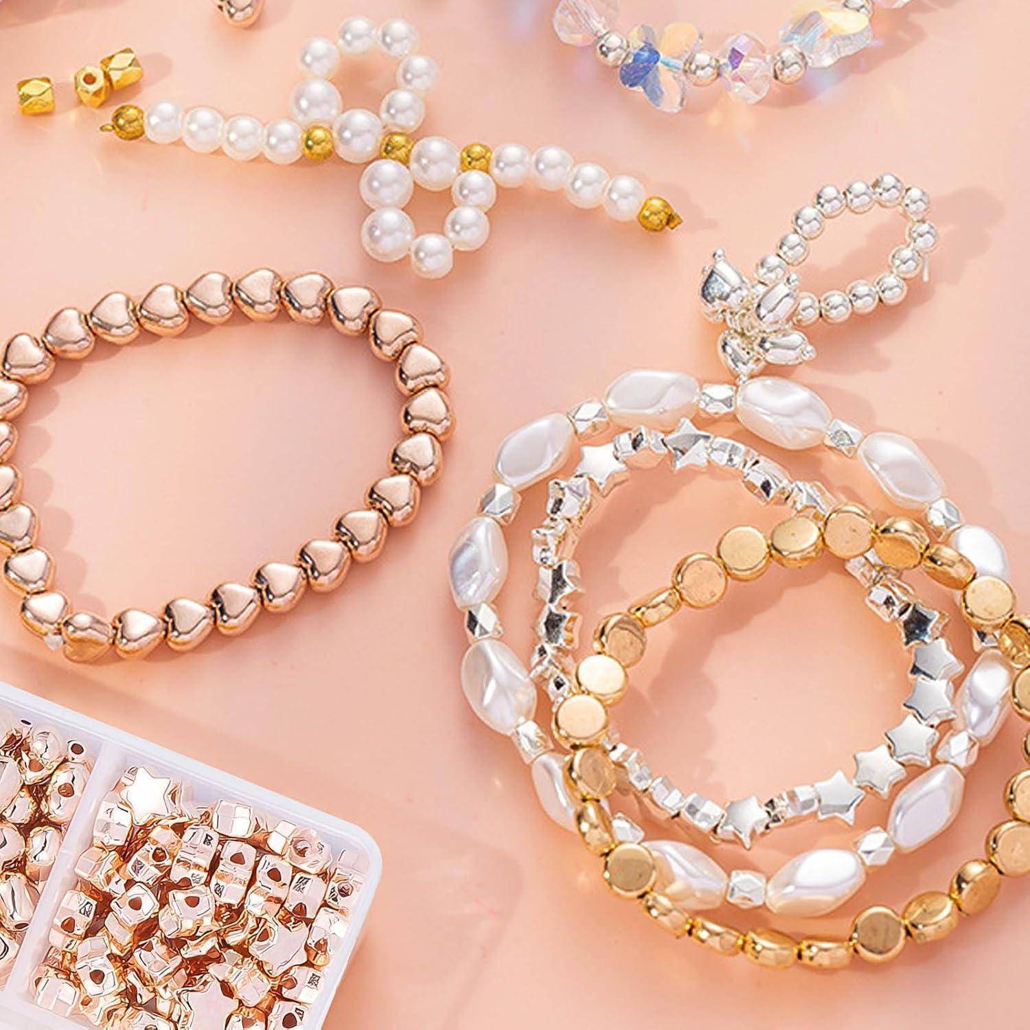 Assortierte Perlen- und Kristallarmbänder sowie Haargummis auf rosafarbenem Hintergrund arrangiert, mit Roségold-, Weiß- und Goldtönen.