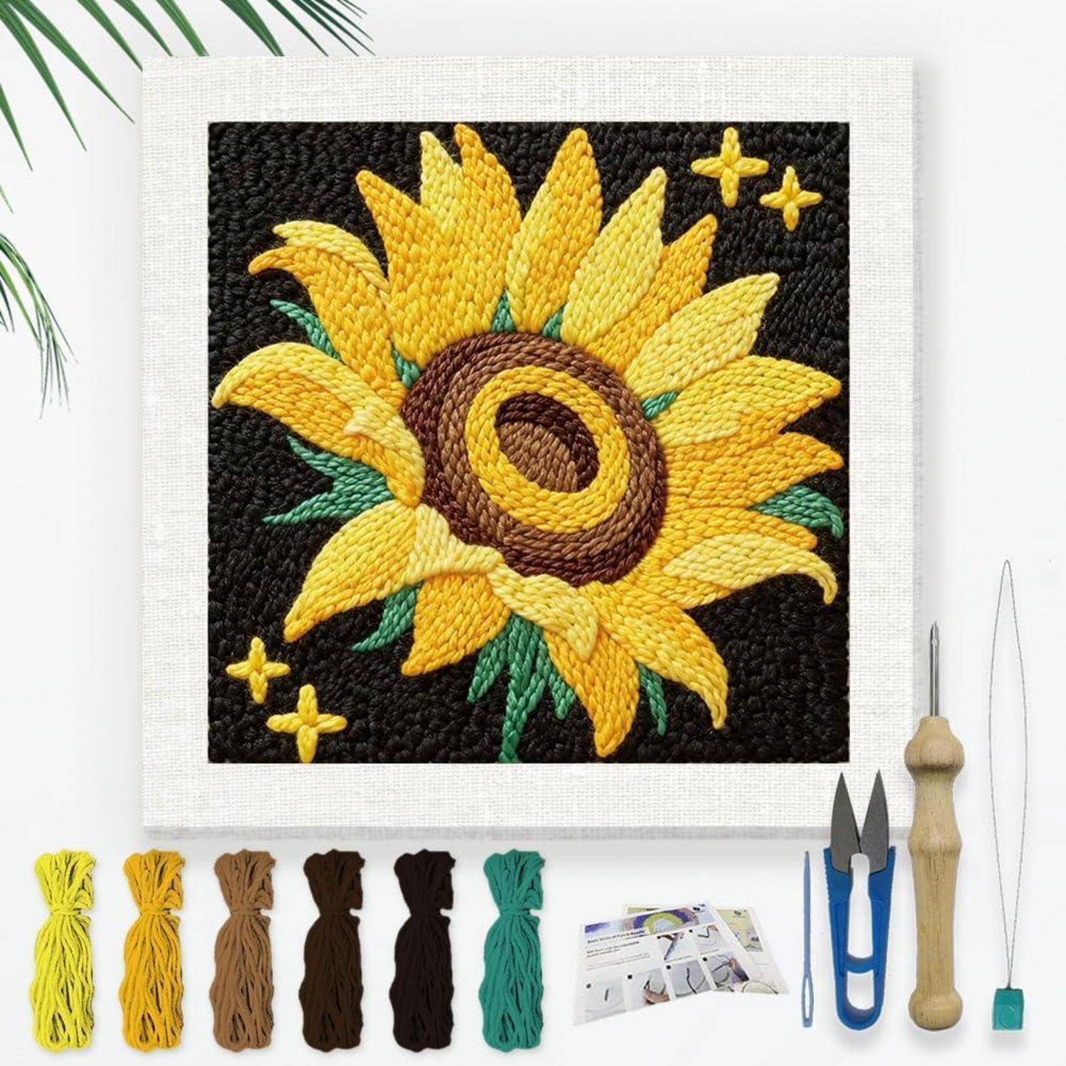 Stickerei-Set mit einem Sonnenblumen-Design auf schwarzem Stoff, mit farbigen Fäden, Werkzeugen und Anleitung, die unter dem fertigen Muster angeordnet sind.
