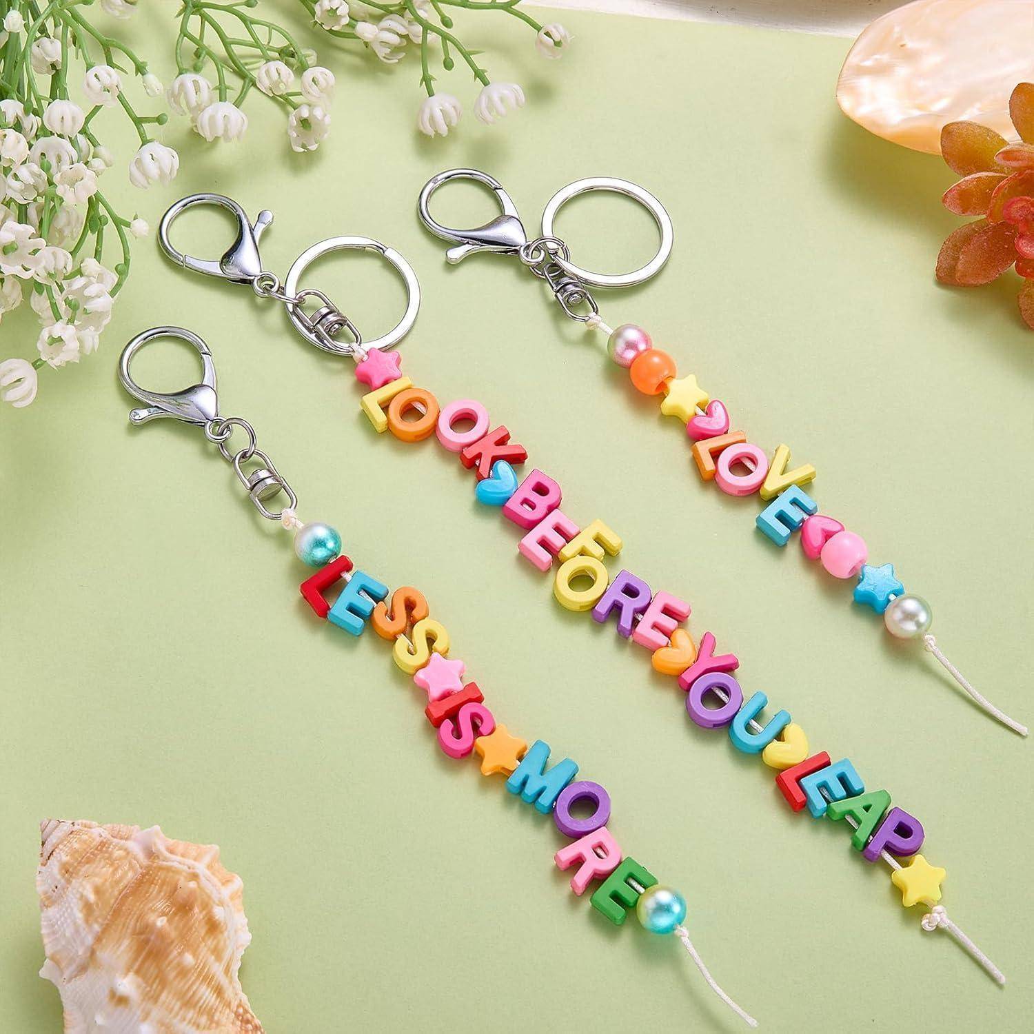 Drei bunte Perlenanhänger mit der Aufschrift „LOOK BEFORE YOU LEAP", „LOVE"" und „LESS IS MORE"" auf hellgrünem Hintergrund.