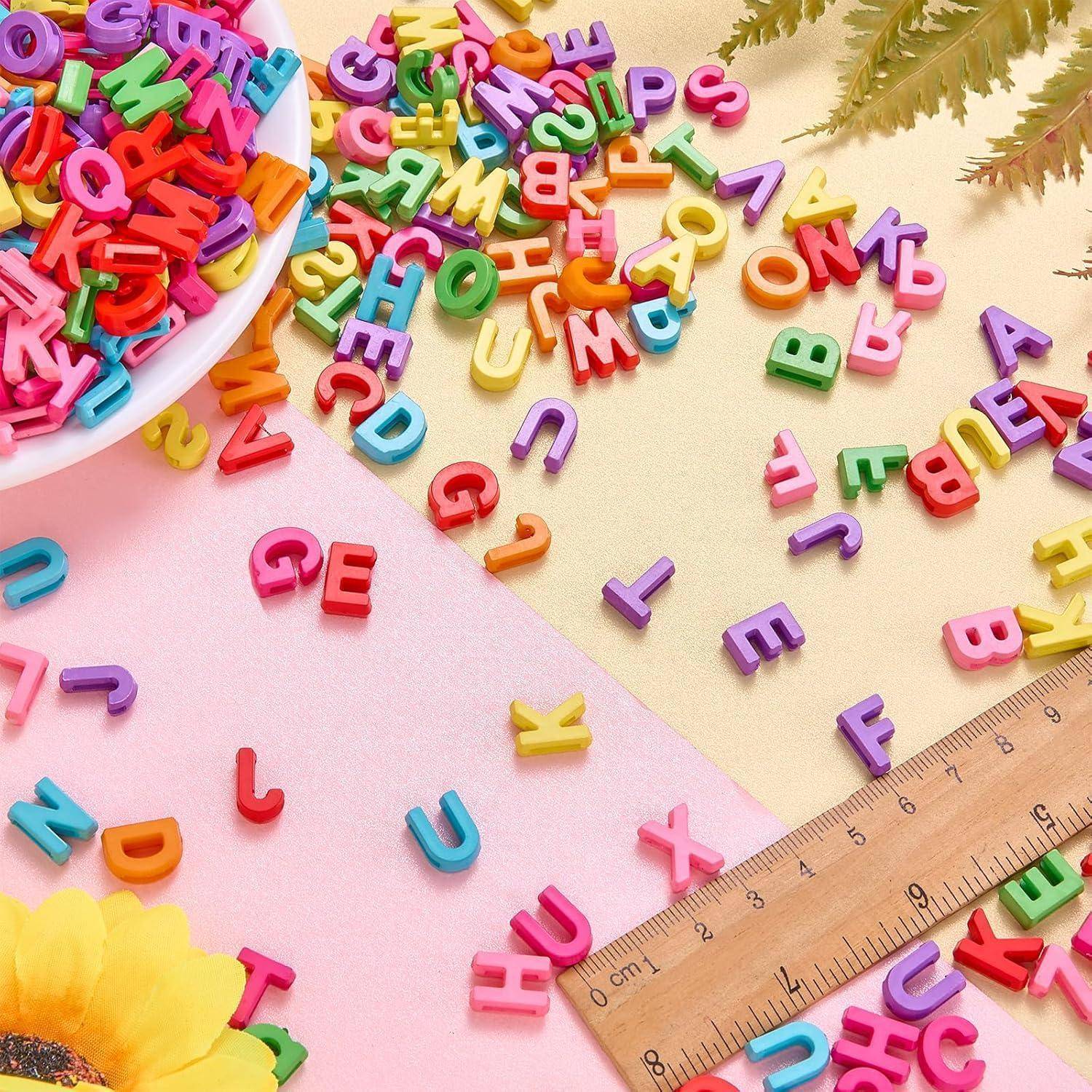 Bunte Kunststoff-Buchstaben verstreut auf Pastellpapier neben einem Holzlineal, mit einer Schale mit Buchstaben und einer gelben Blume.