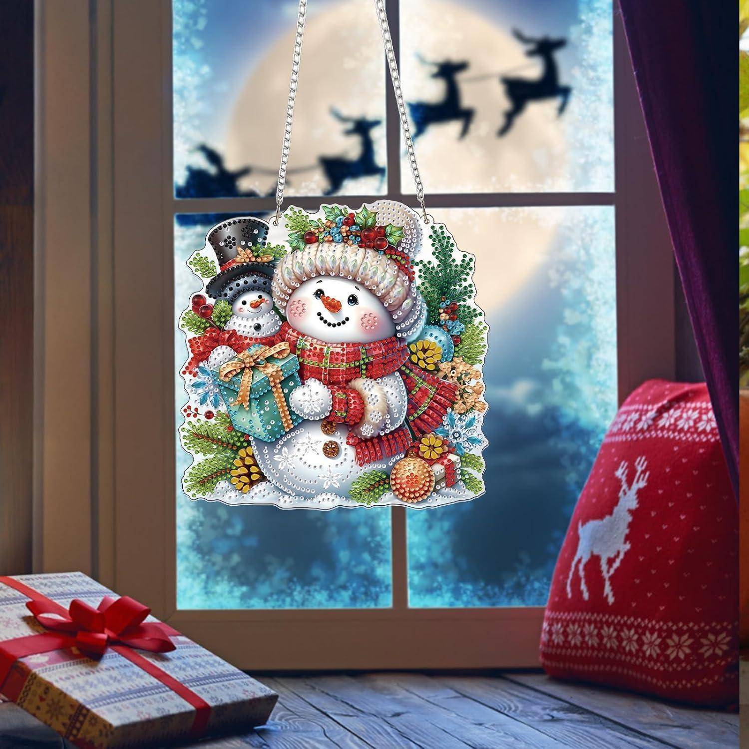 Weihnachtlicher Schneemann-Schmuck, der in einem Fenster hängt, mit einem Geschenk und einem roten Winterpullover daneben; schneebedeckte Außenszene dahinter.