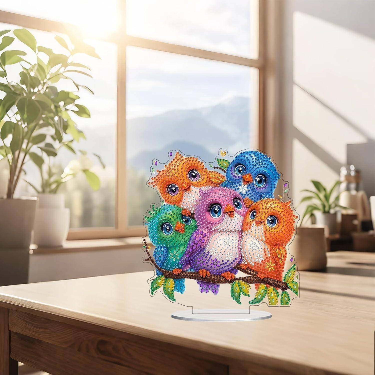 Farbenfrohe vogelförmige Kristalltischtop-Verzierung mit fünf Cartoon-Vögeln auf einem Ast, ausgestellt auf einem Holztisch in einem hellen, sonnendurchfluteten Raum.