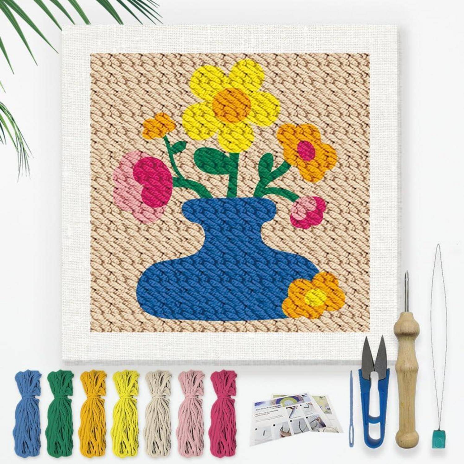 Needlepoint-Set mit einem farbenfrohen Blumenvasenmotiv, mit Wollsträngen, Werkzeugen und Anleitung, die unter der fertigen Leinwand angeordnet sind.