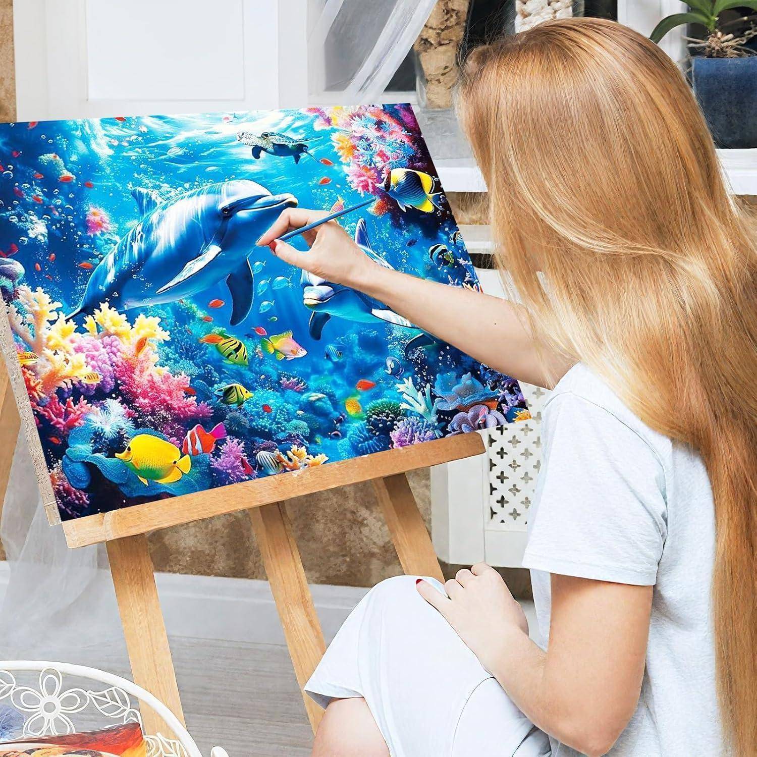 Frau malt eine bunte Unterwasserszene mit einem Delphin und tropischen Fischen auf einer Staffelei.