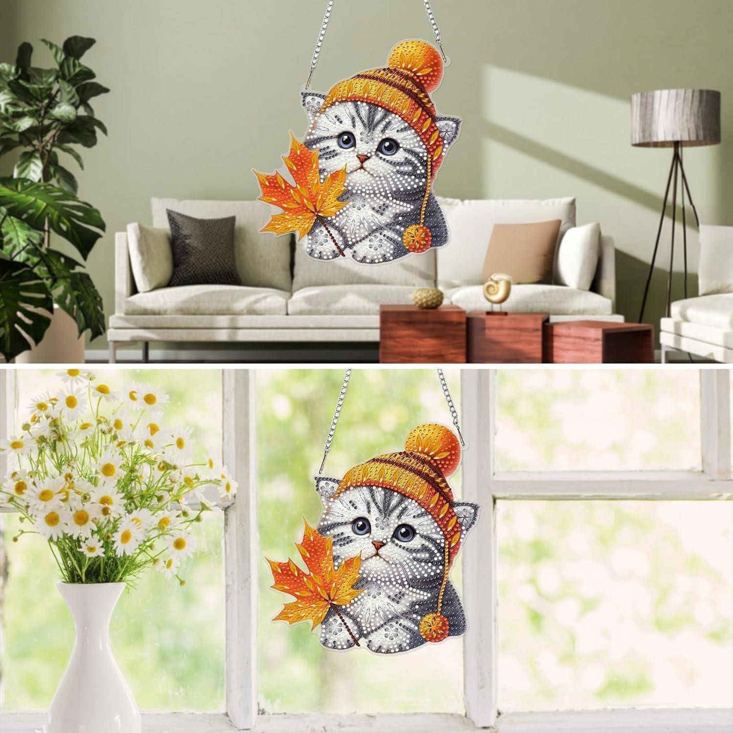Funkelnde kätzchen-förmige hängende Dekoration mit einem Herbstblatt und einer Strickmütze, gezeigt in einem Wohnzimmer und an einem Fenster.