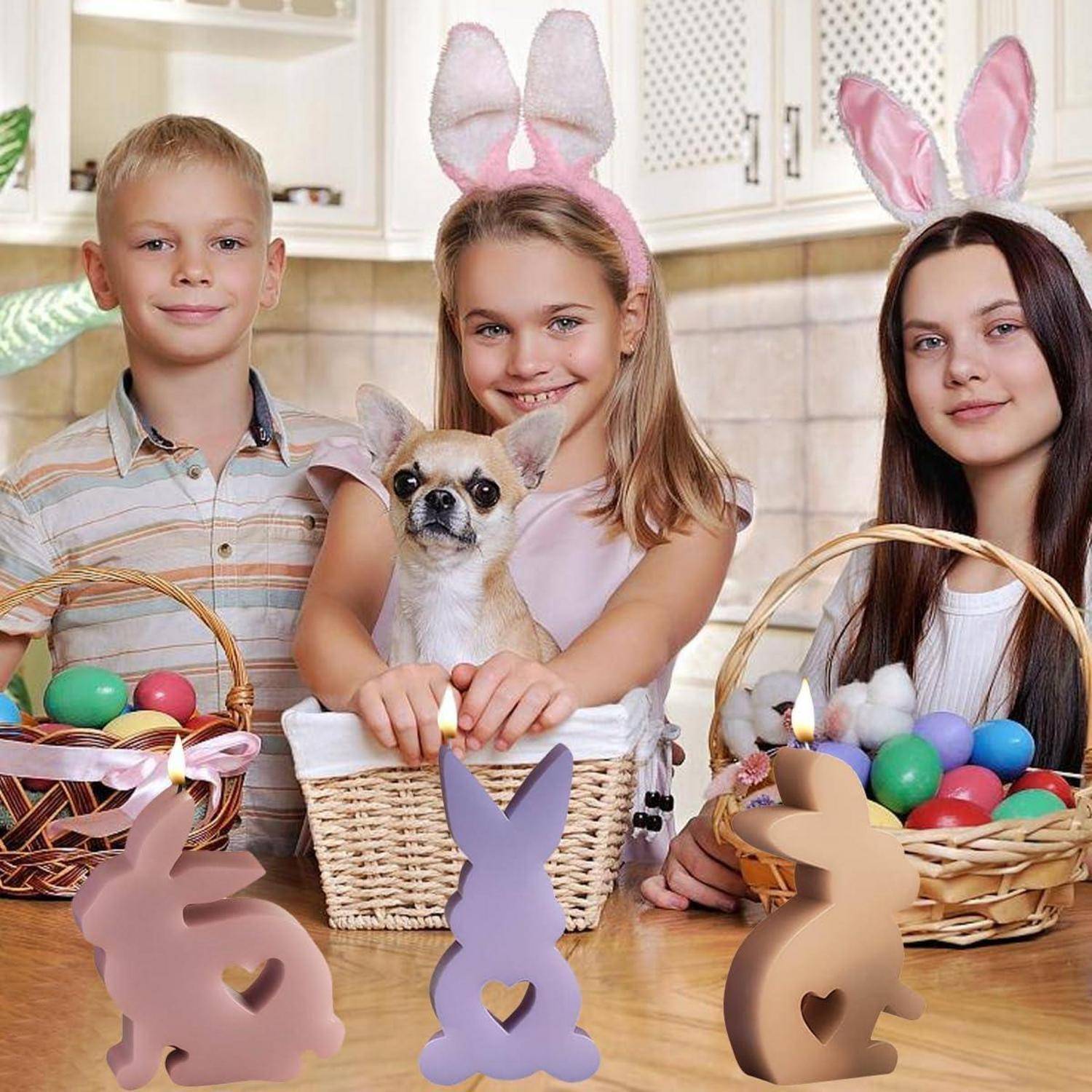 Drei Kinder mit Hasenohren posieren in einer Küche mit einem kleinen Hund in einem Korb und Ostereiern in geflochtenen Körben auf dem Tisch.