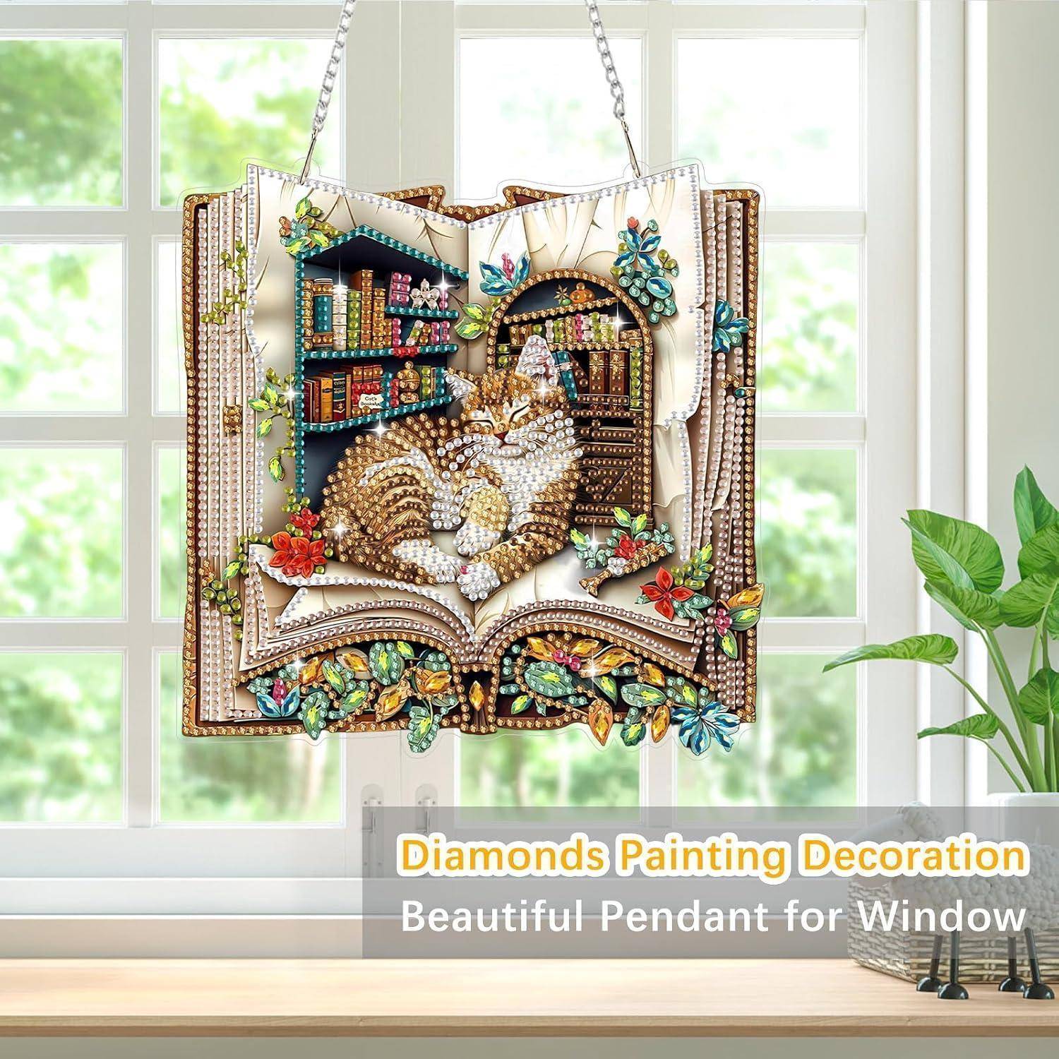Dekoratives hängendes Diamantmalerei-Bild einer Katze, die in einem offenen Buch zusammengekuelt ist, mit Schmetterlingen und Blumen, ausgestellt als Fensteranhänger.