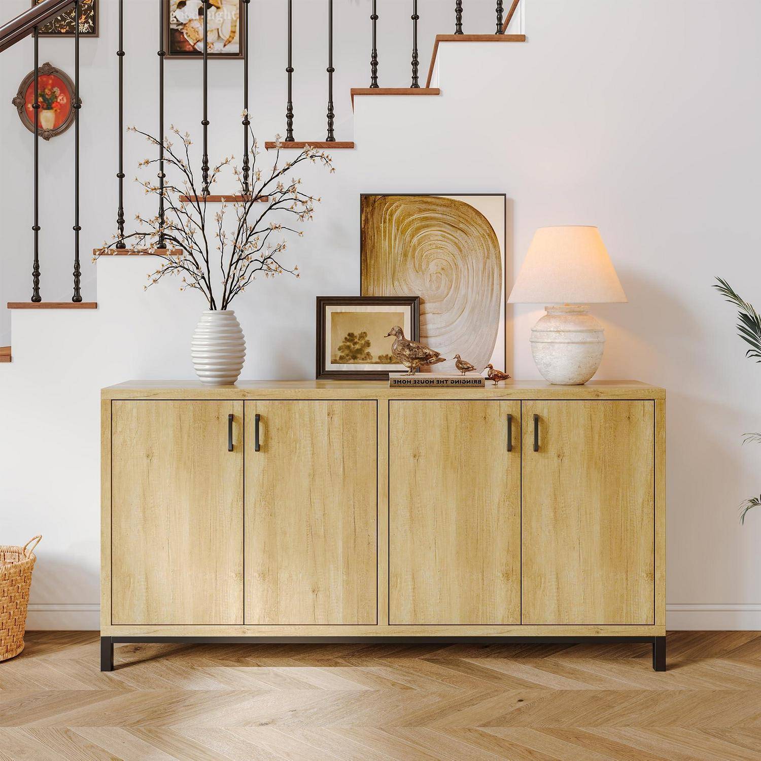 Holzkommode unter einer Treppe, gestaltet mit einer Vase, gerahmter Kunst, kleiner Dekoration und einer leuchtenden Tischleuchte in einem hellen Wohnzimmer.