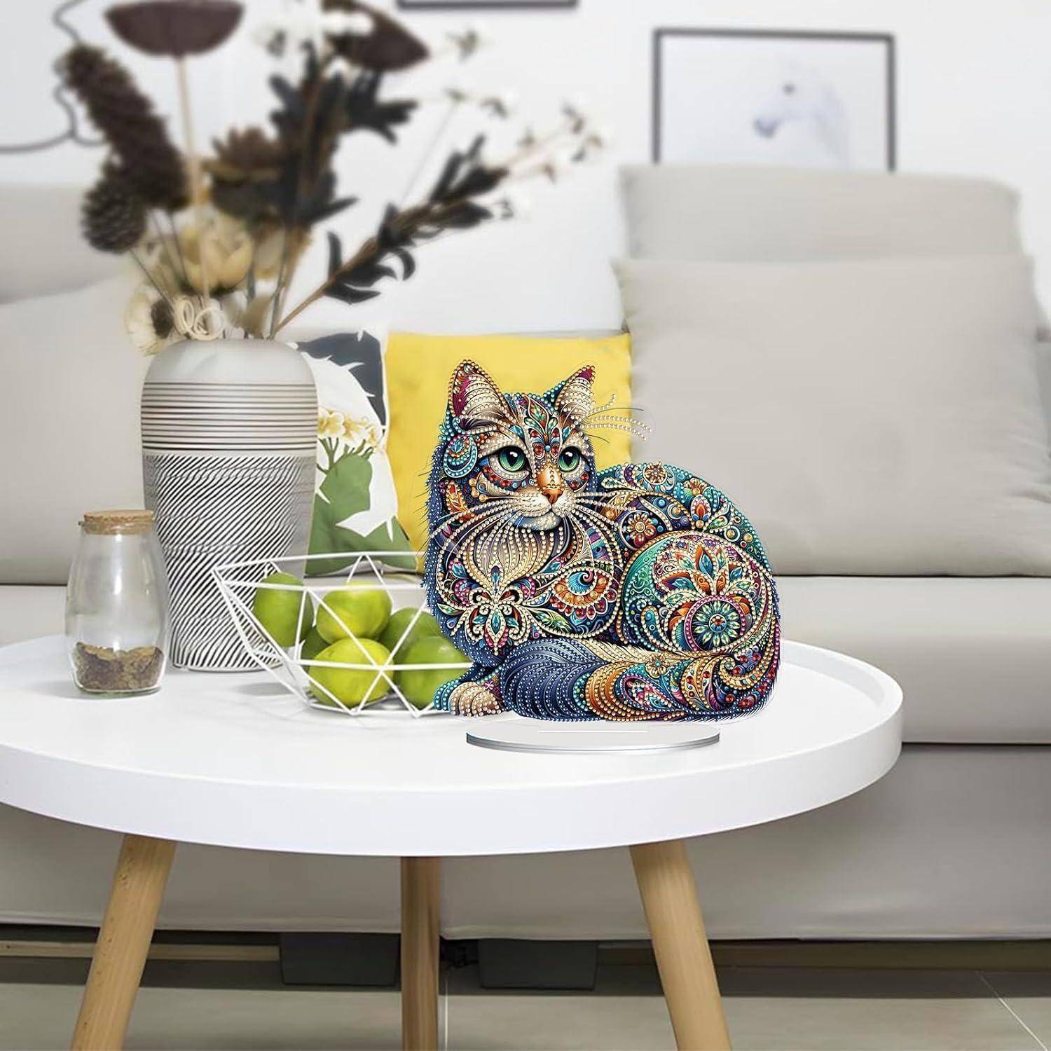Dekorative Katzenskulptur mit buntem Mosaikmuster auf einem weißen Couchtisch, neben einer Vase mit Trockenblumen, einer Drahtobstschale und einem Sofa.