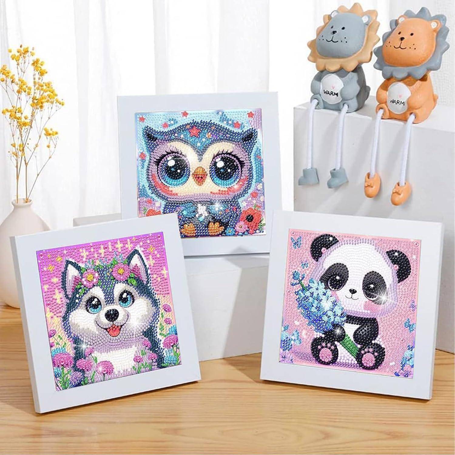 Drei gerahmte Diamantmalerei-Tierbilder – Husky, Eule und Panda – auf einem Tisch ausgestellt, mit zwei kleinen Löwen-Plüschtieren im Hintergrund.