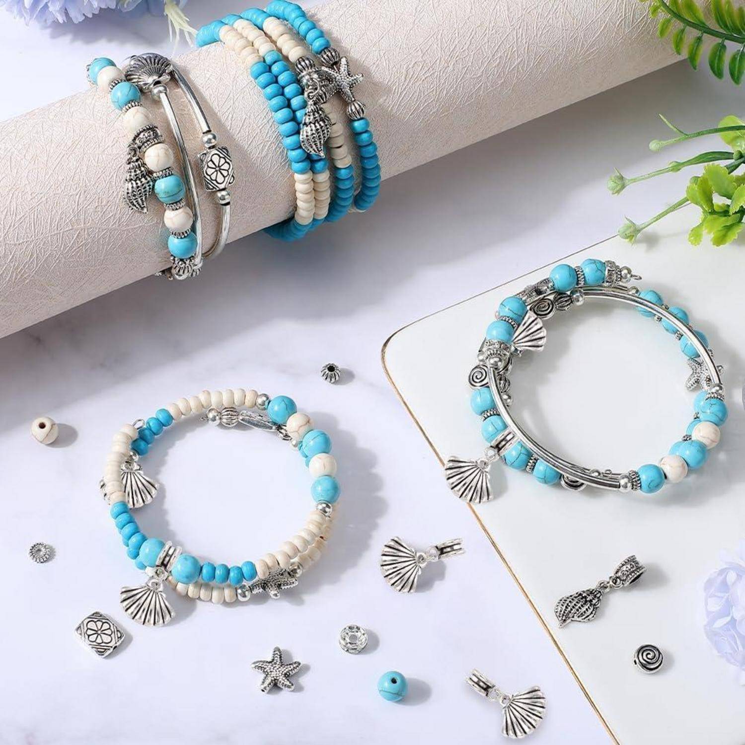 Silberarmband mit Perlen und Anhängern in Türkis, Weiß und Grau werden auf einer weißen Oberfläche mit kleinen losen dekorativen Anhängern präsentiert.