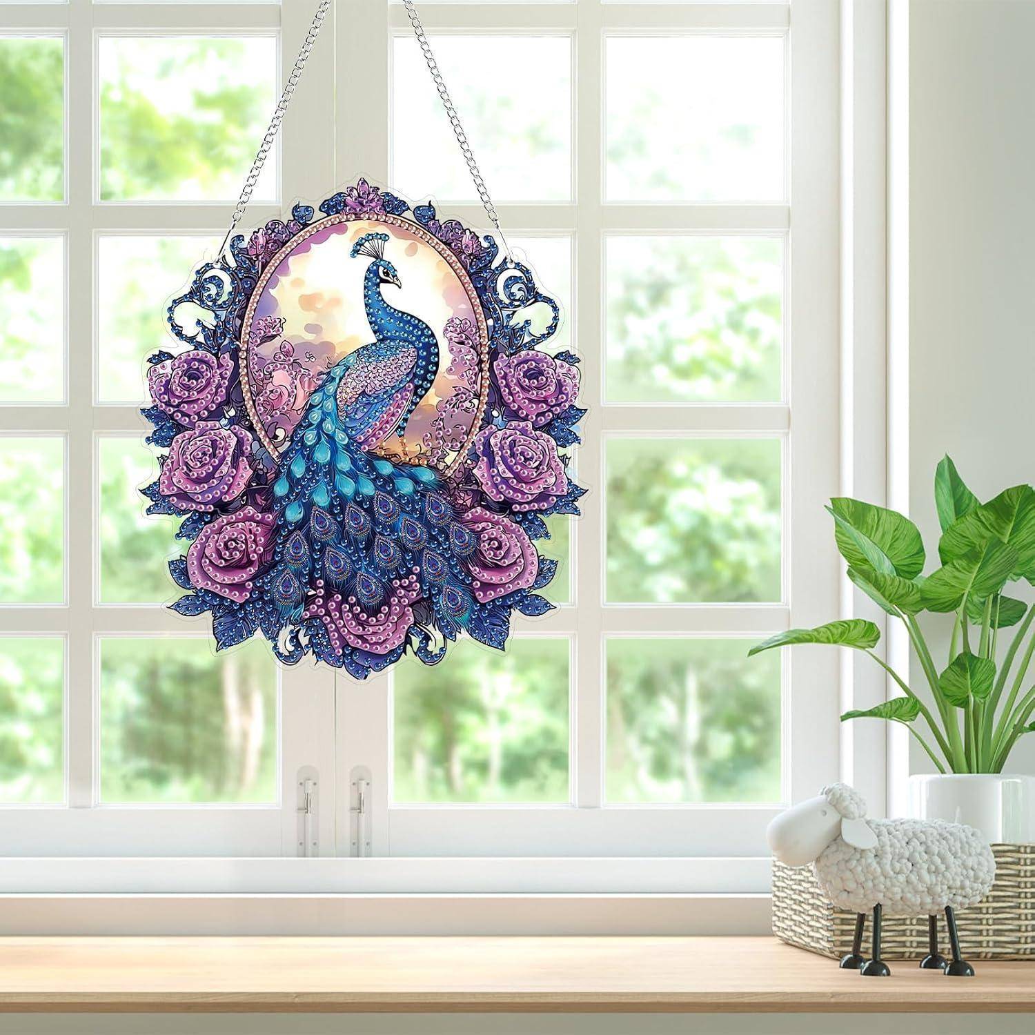 Pfauenmotiv-Wandkunst zum Aufhängen mit violetten Rosen und einem blauen Pfau, ausgestellt in einem hellen Fenster über einer Fensterbank mit einer Pflanze und einer kleinen Schaffigur.