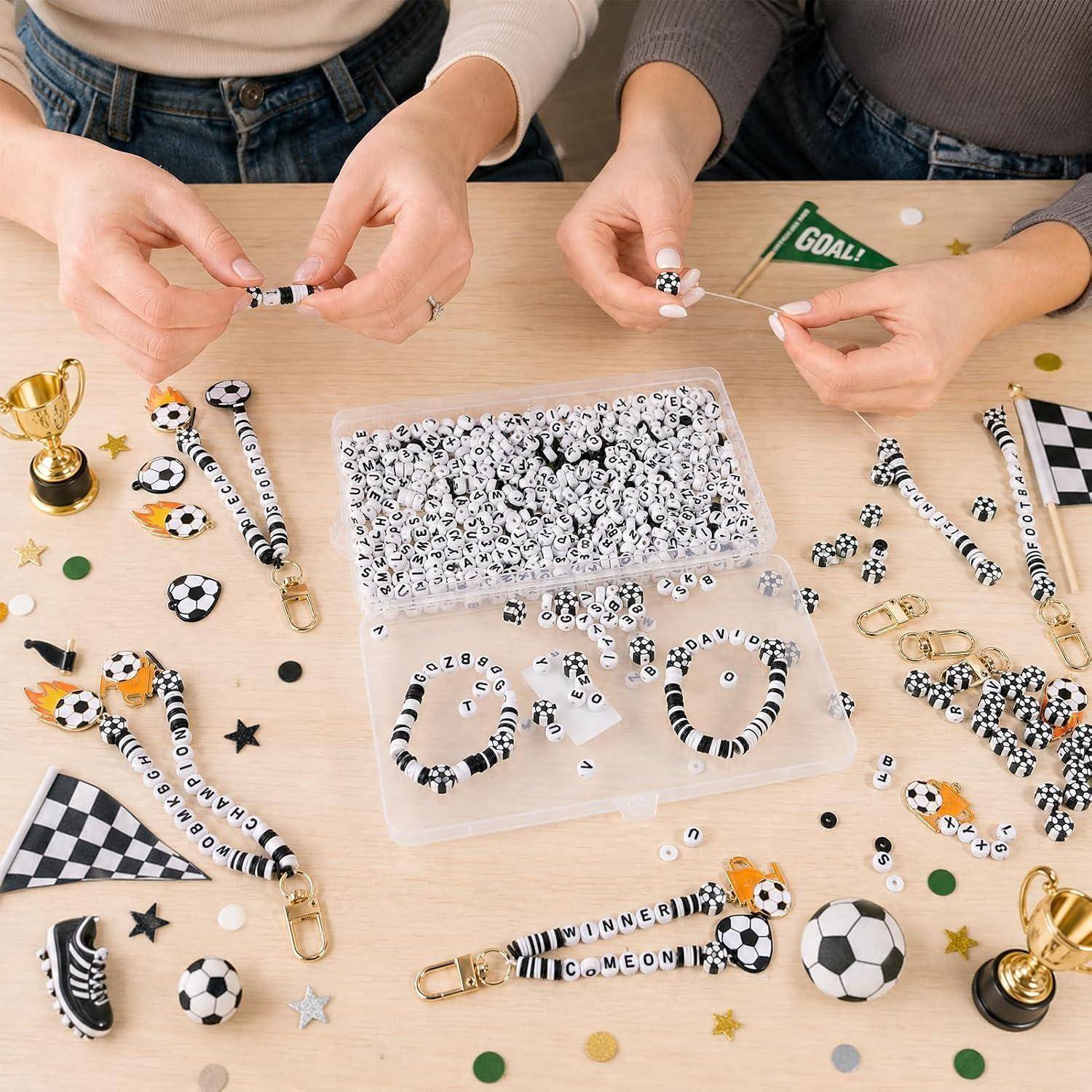 Menschen stellen gestreifte Fußball-Perlenanhänger an einem Basteltisch mit Behältern voller Perlen, fertigen Anhängern und kleinen Pokaldekorationen zusammen.
