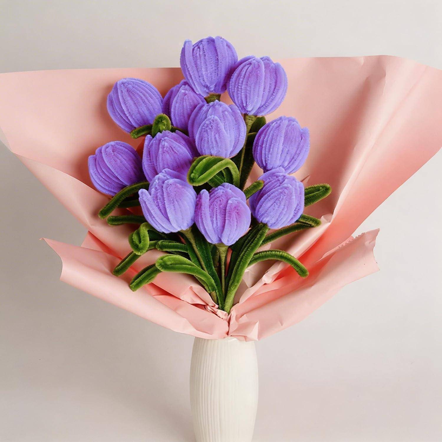 Strauß aus violetten Tulpen in rosa Papier eingewickelt in einer weißen Vase vor einem einfachen, hellen Hintergrund.