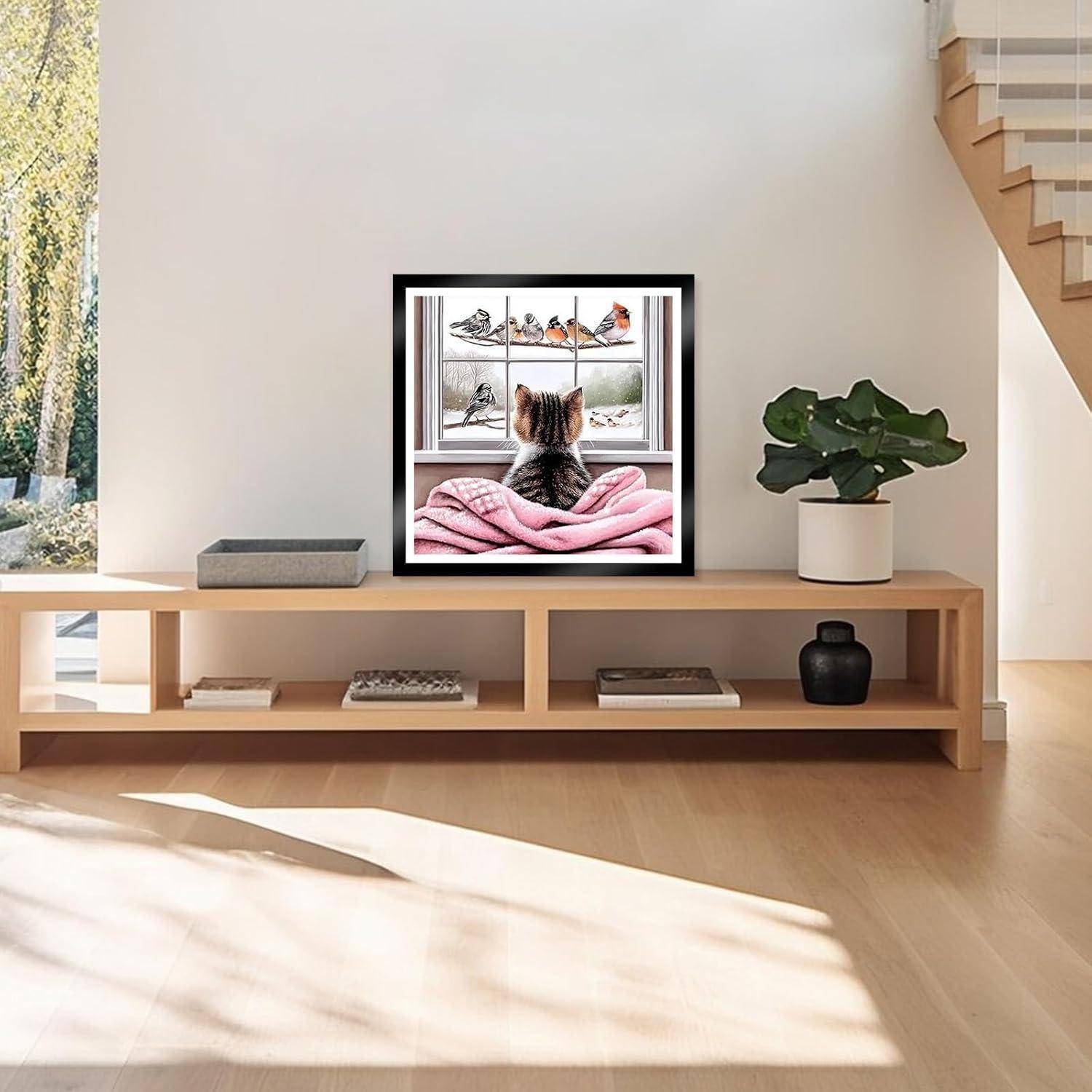 Gerahmtes Foto einer Katze auf einer rosa Decke, die Vögel am Fenster beobachtet, ausgestellt auf einem niedrigen hölzernen Sideboard in einem hellen Wohnzimmer.