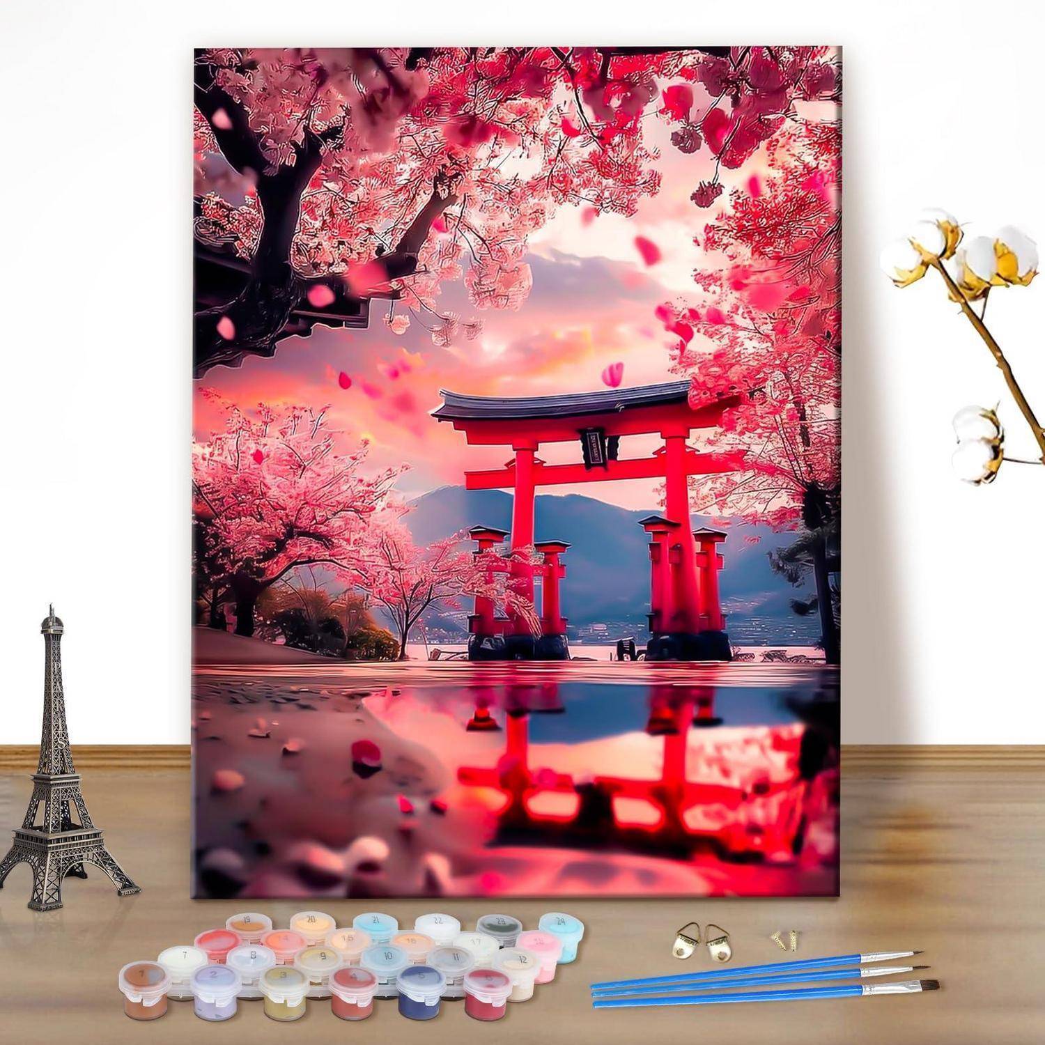Ein Druck eines roten Torii-Tors unter rosa Kirschblüten bei Sonnenuntergang, gespiegelt im Wasser, auf einer Staffelei ausgestellt mit Kunstbedarf in der Nähe.